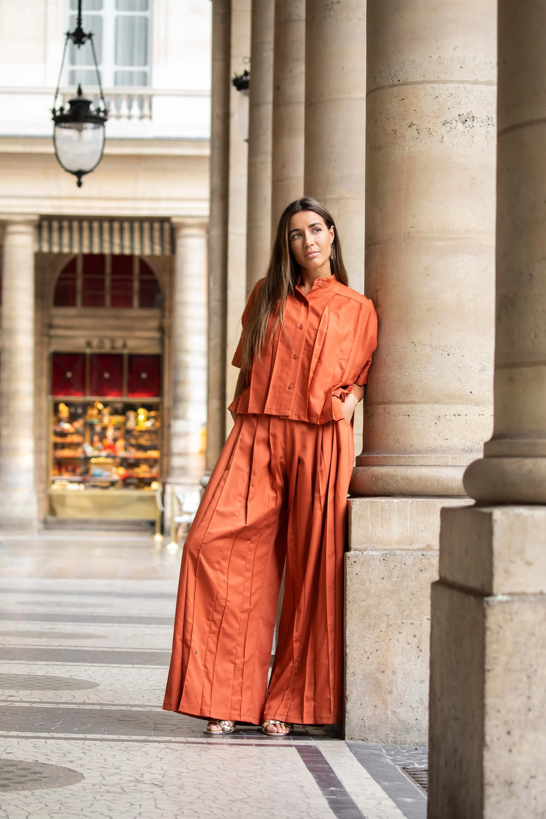 Femme en mode orange posant près de colonnes architecturales