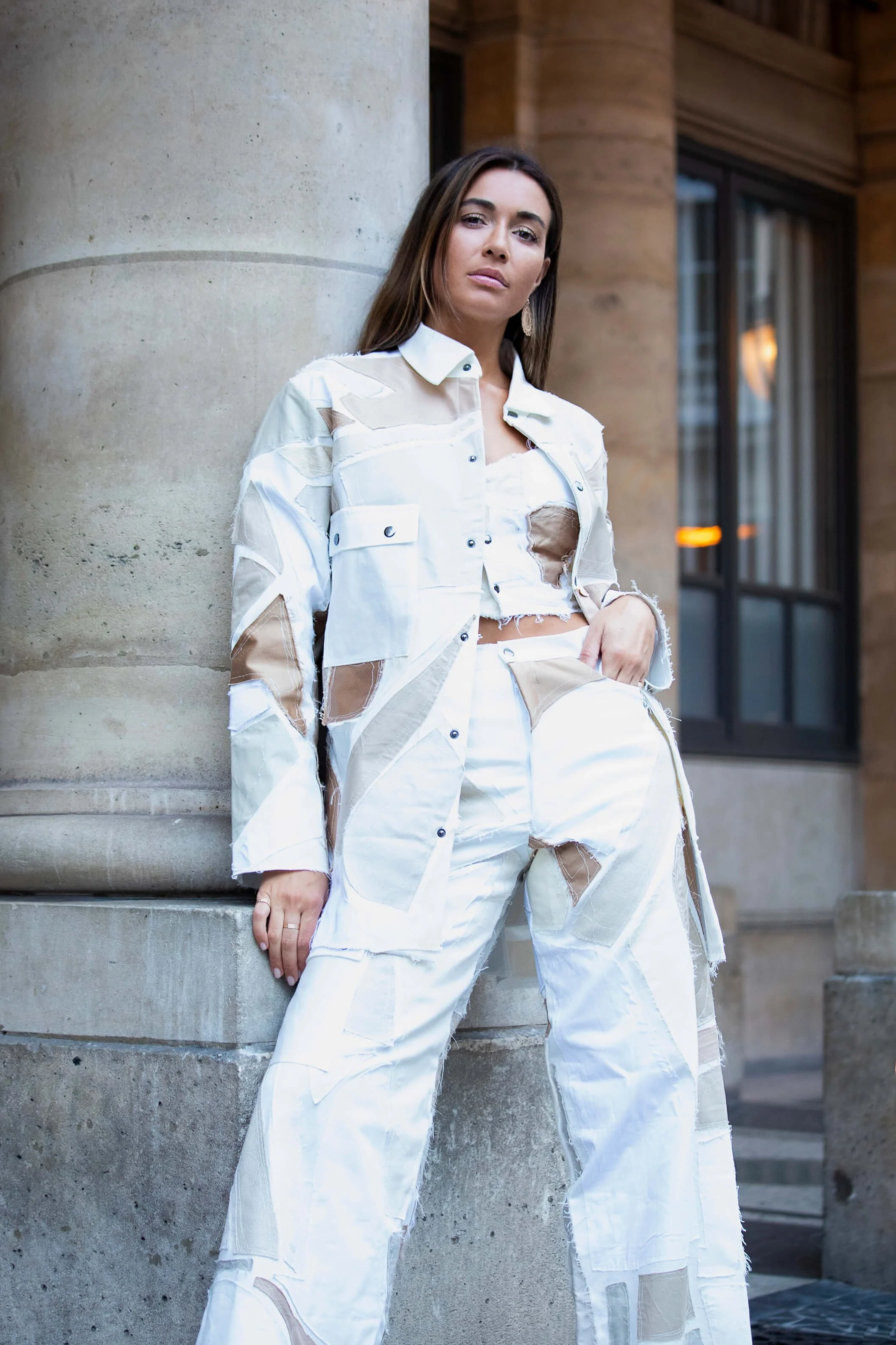 Femme portant une tenue urbaine chic en blanc et beige, posant près d'une colonne.