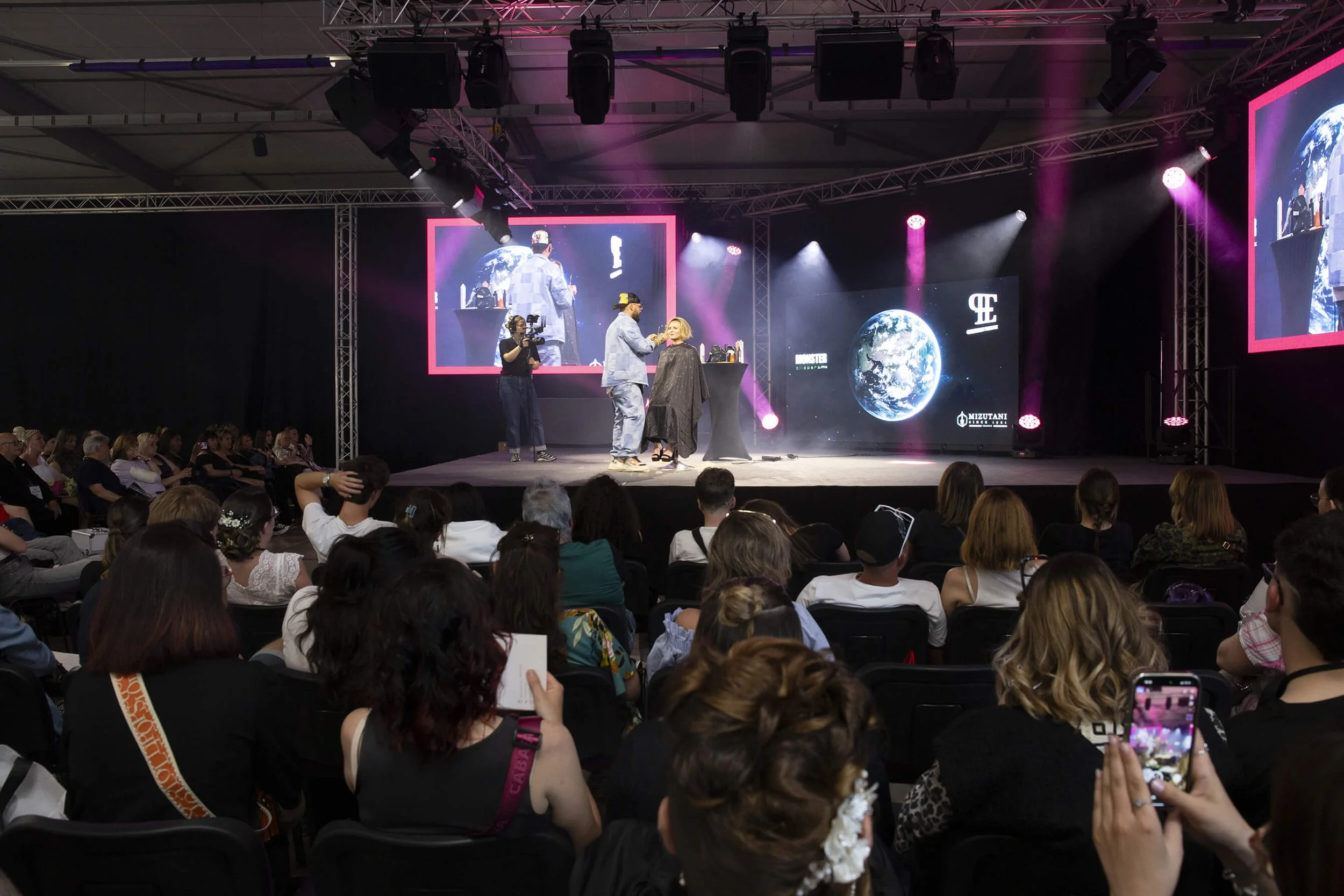 Un photographe professionnel capture l'art de la coiffure sur scène avec des éclairages colorés. Un styliste en action, démontrant des techniques de coiffure devant un public admiratif.