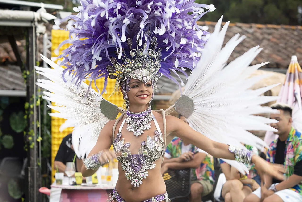 François Fauré immortalise une danseuse en costume flamboyant, orné de plumes violettes et de bijoux scintillants, lors d’un événement culturel.  Son style photographique unique capture la vivacité et les couleurs éclatantes de la performance, avec u
