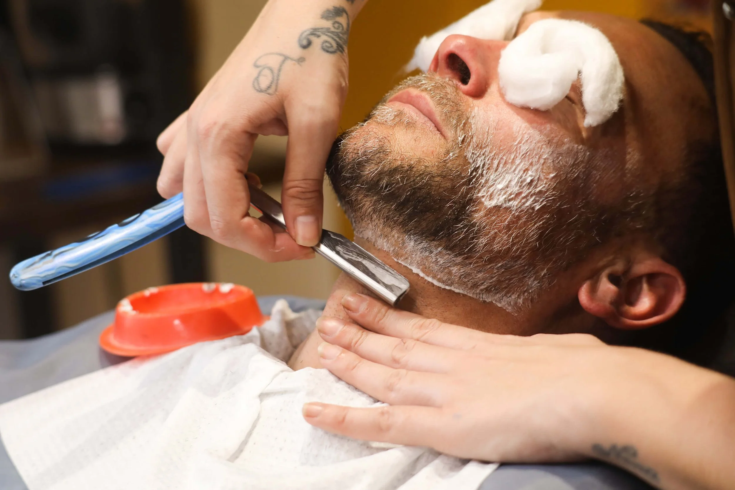 Un homme recevant un rasage professionnel avec un rasoir en main, entouré de serviettes et de produits de soin.
Un salon de rasage professionnel, mettant en avant les accessoires et l'atmosphère relaxante.
Un homme se détendant pendant un soin de bar