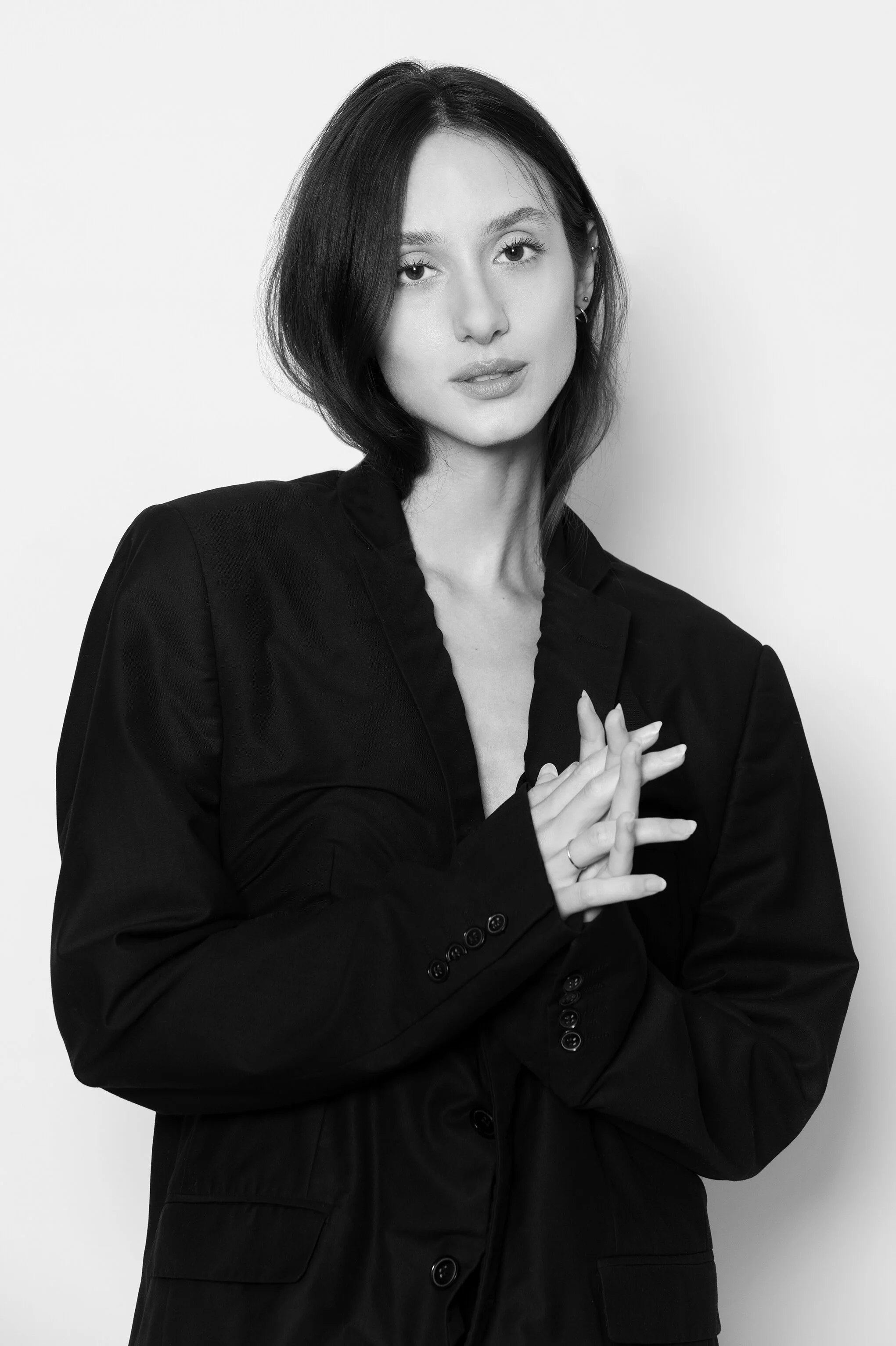 Portrait en noir et blanc d'une femme avec des cheveux courts, portant une veste noire, regardant vers l'appareil, mains jointes