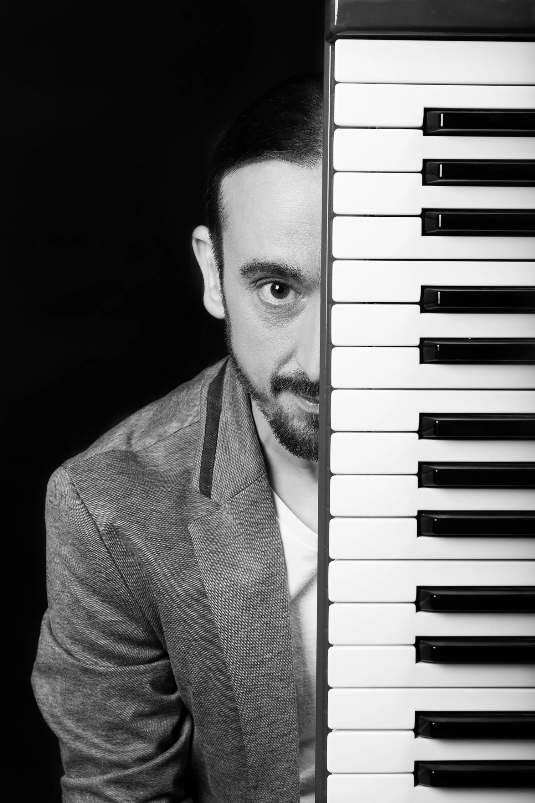 Portrait en noir et blanc de François Fauré, photographe professionnel, avec un homme se cachant derrière un piano.  Le style photographique de François Fauré met en avant des couleurs et des objets artistiques.  L’ambiance en noir et blanc capturée 