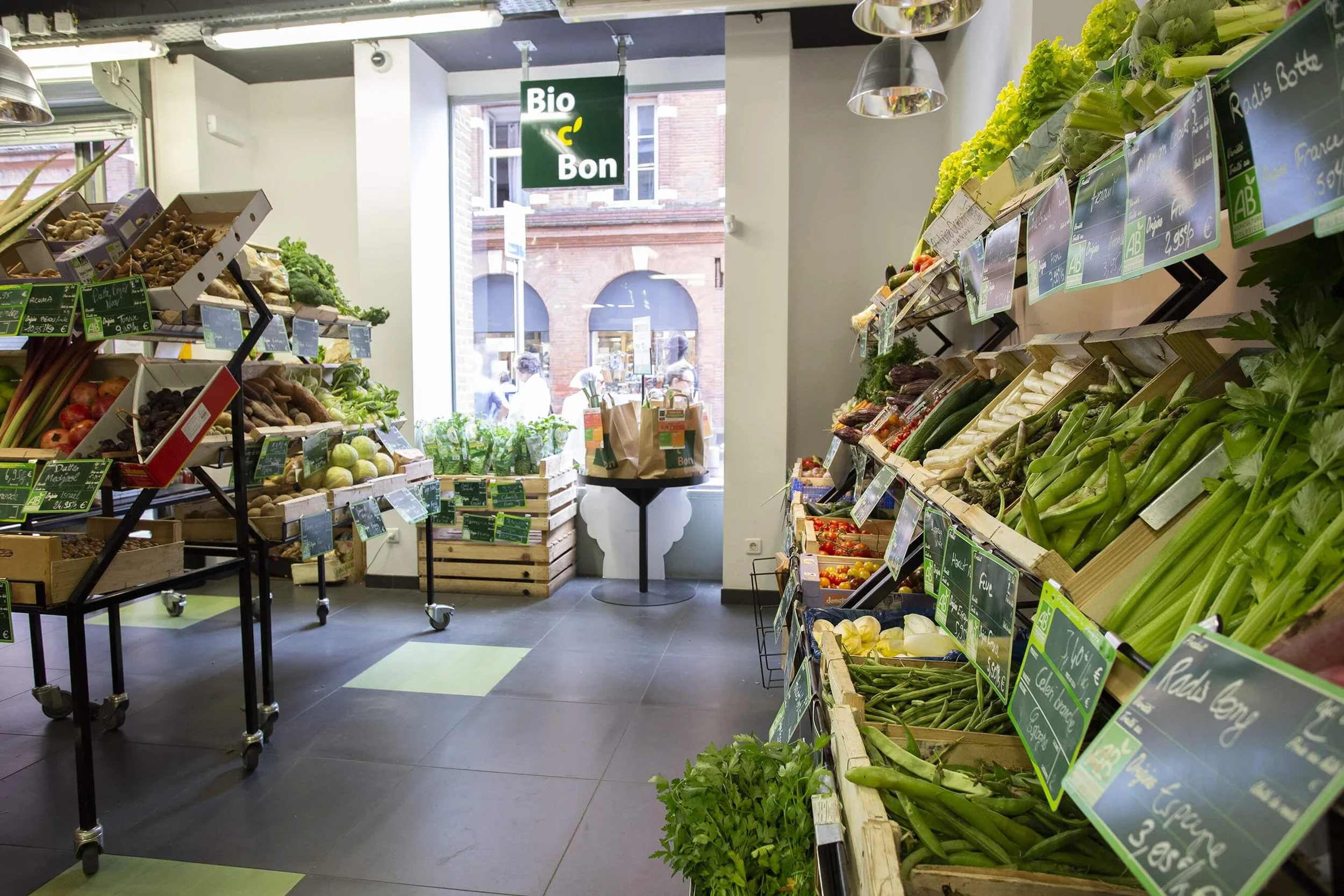 Ce magasin Bio offre une ambiance chaleureuse et accueillante, mettant en avant une sélection variée de produits frais. Les étagères sont soigneusement organisées, présentant des légumes colorés et des étiquettes de prix claires. Le décor moderne et 