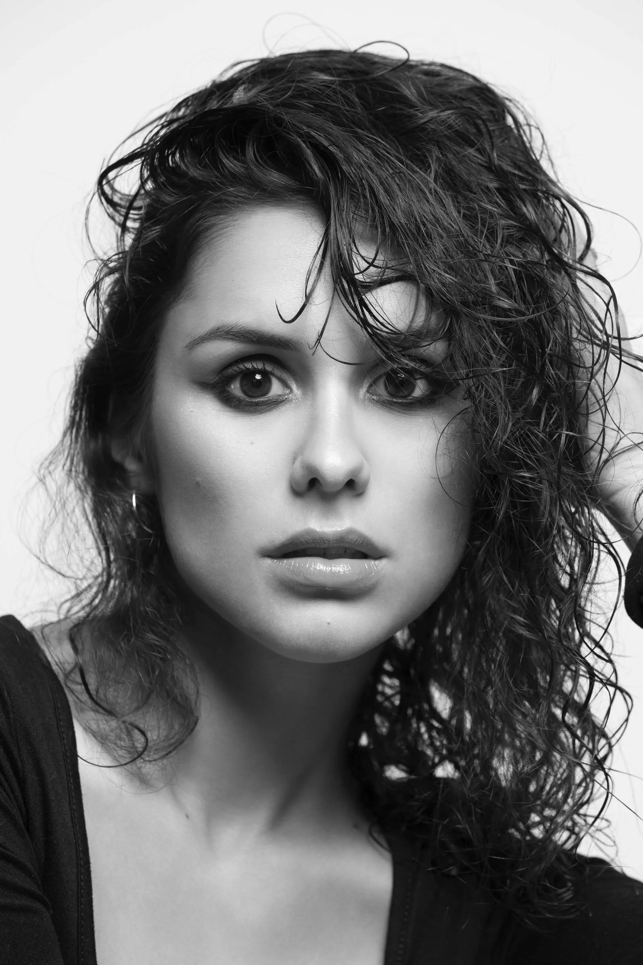 Portrait en noir et blanc d'une femme avec des cheveux bouclés et une expression sérieuse, portant un haut sombre.