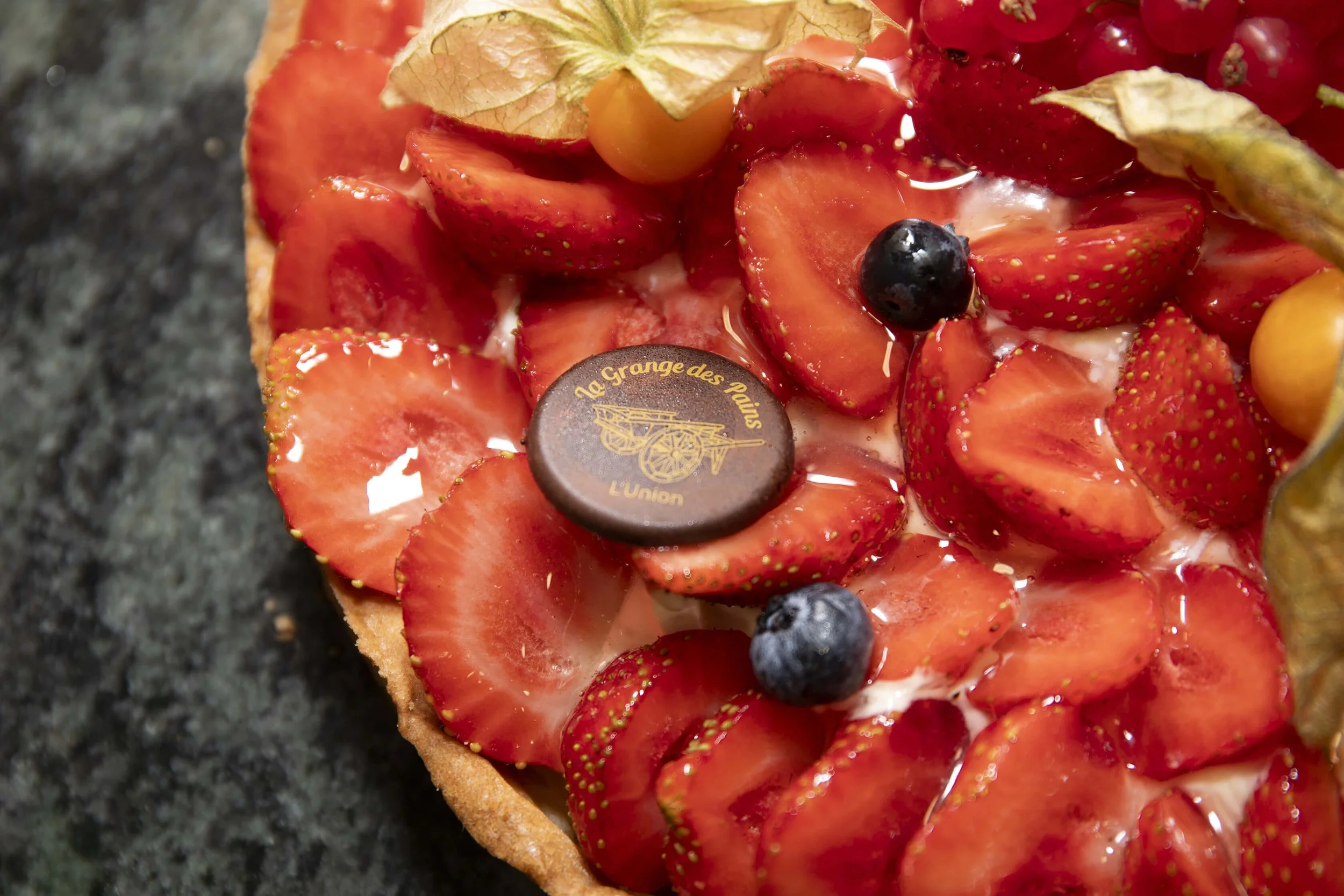 Une tarte aux fraises et fruits rouges, sublimée par un décor raffiné, est mise en valeur par une photographie artistique.  Cette image saisit les couleurs vives et la texture appétissante de la tarte, mettant en avant la qualité des ingrédients frai