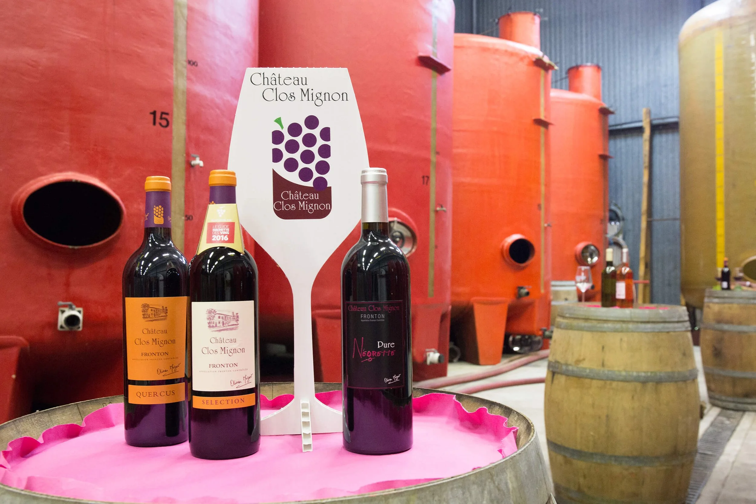 Vins rouges du Château Clos Mignon exposés dans une cave moderne aux cuves colorées.