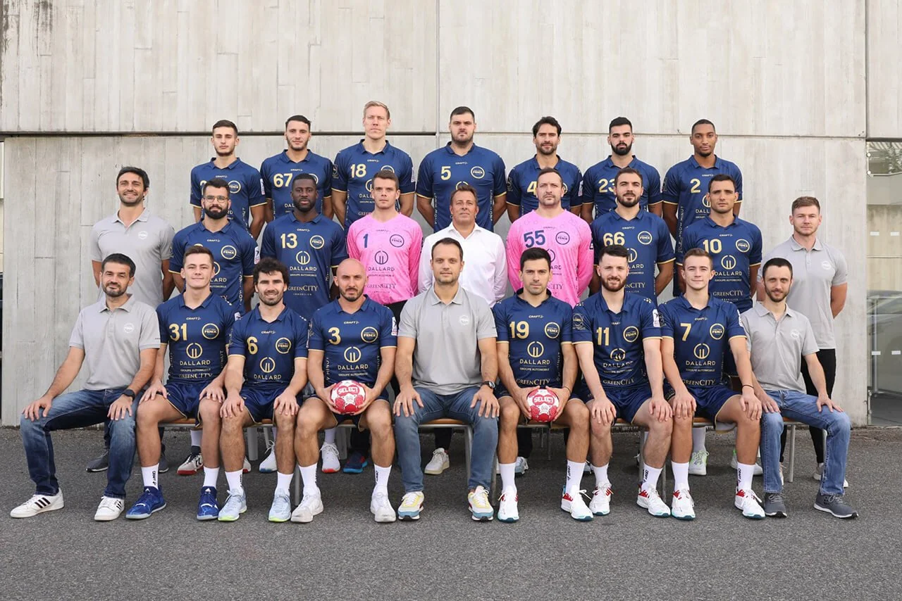 Photo de l'équipe de handball avec des joueurs en maillots bleus et un décor moderne.
Portrait collectif des joueurs de handball posant ensemble dans un environnement urbain.
Équipe professionnelle de handball, vêtue de maillots de compétition, devan
