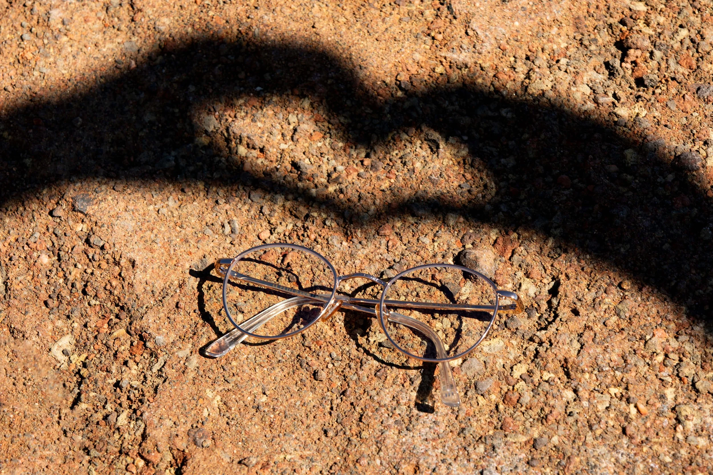 Lunettes transparentes sur un fond de sable avec une ombre de deux mains en forme de cœur.