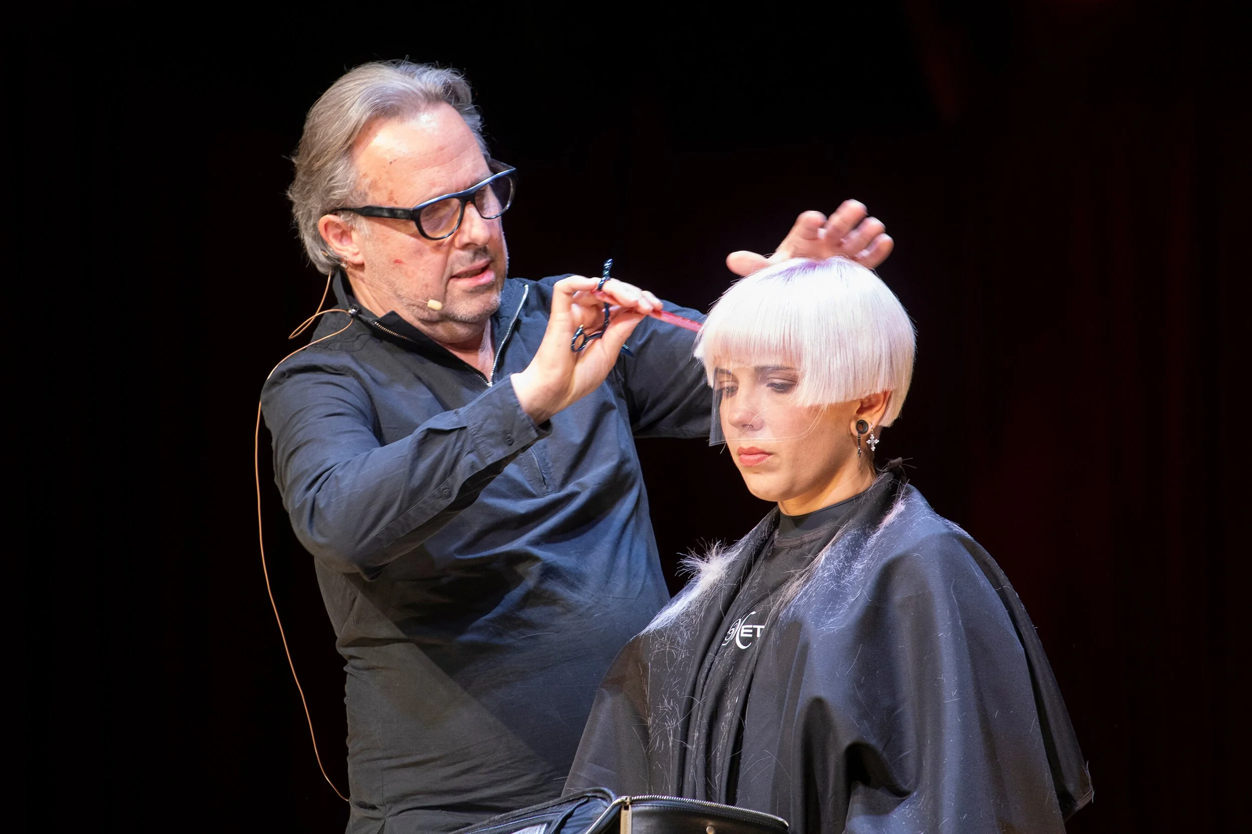 Photographie d'un professionnel de la coiffure en action, mettant en valeur le style et la technique.
Un coiffeur en train de couper les cheveux d'un modèle, illustrant l'art de la coiffure.
Décor de scène avec des couleurs de cheveux modernes, repré