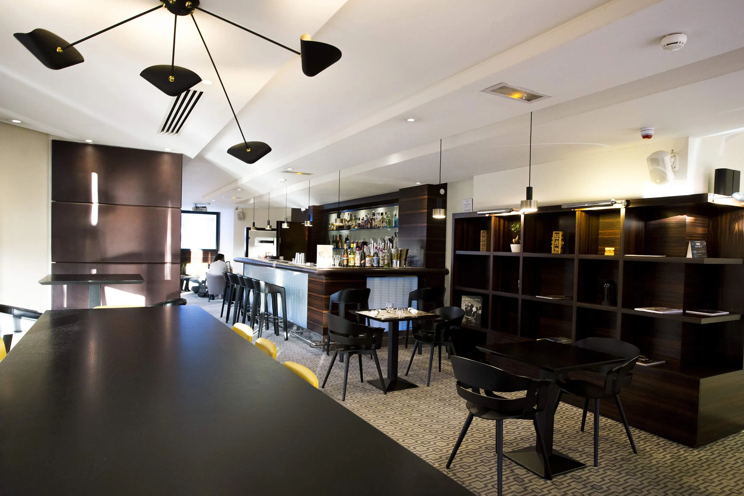 Décor moderne d’un bar, photographié par François Fauré, avec un éclairage élégant et un mobilier contemporain. Les chaises noires contrastent avec les lumières suspendues, créant une ambiance professionnelle et raffinée.  Le style photographique de 