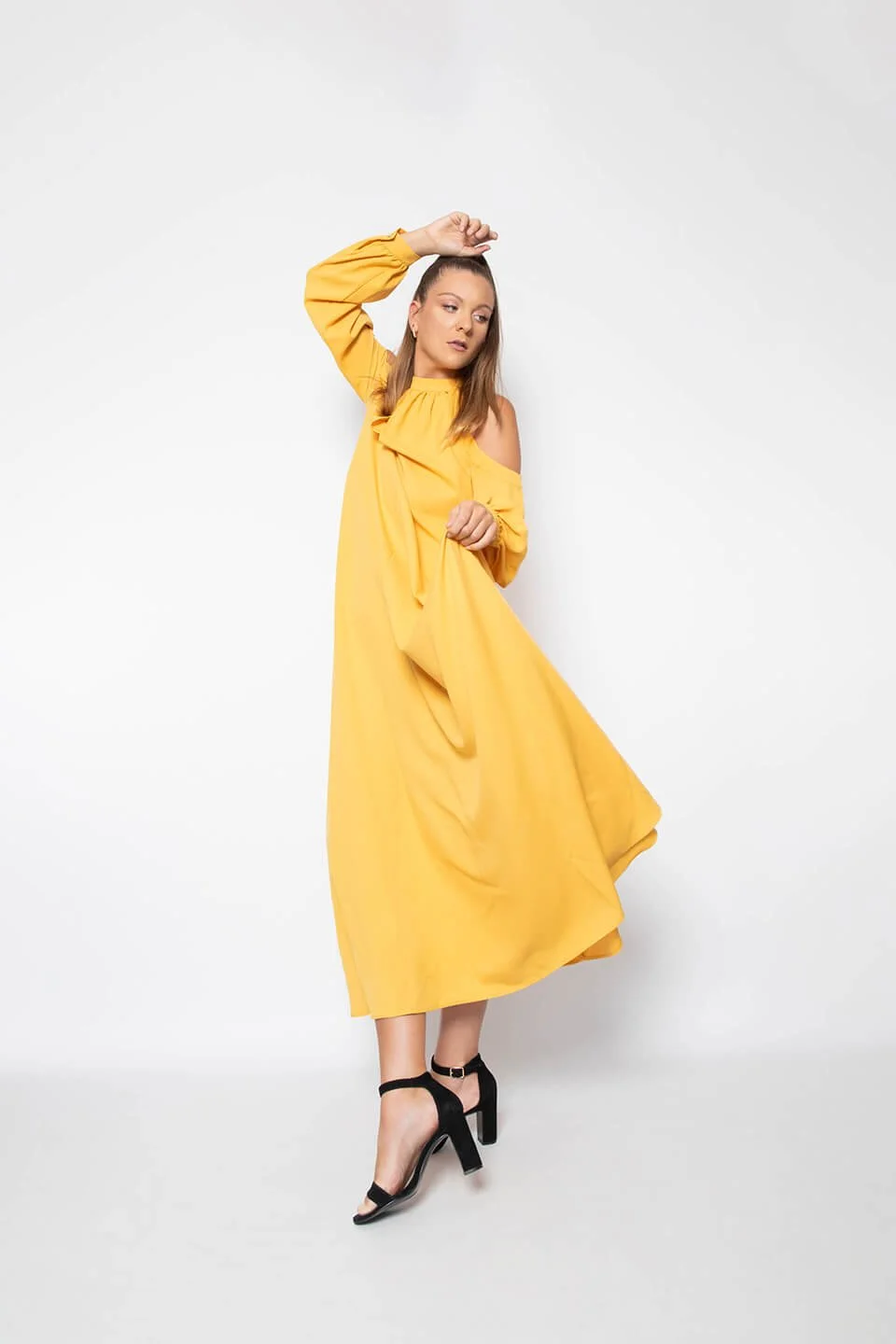 Modèle féminin en robe jaune avec des sandales noires. Pose en Studio