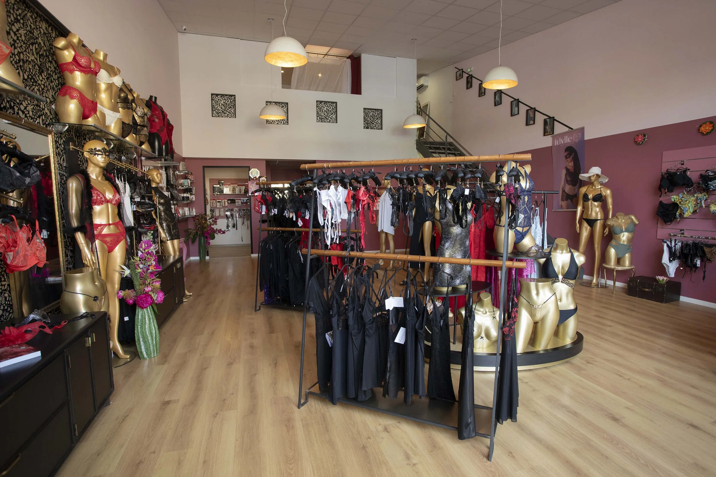 Photographie professionnelle d’une boutique de lingerie, mettant en valeur son décor moderne et ses couleurs vives.  L’ambiance chaleureuse et les étagères soigneusement organisées créent une atmosphère invitante.  Des mannequins en or subliment la p