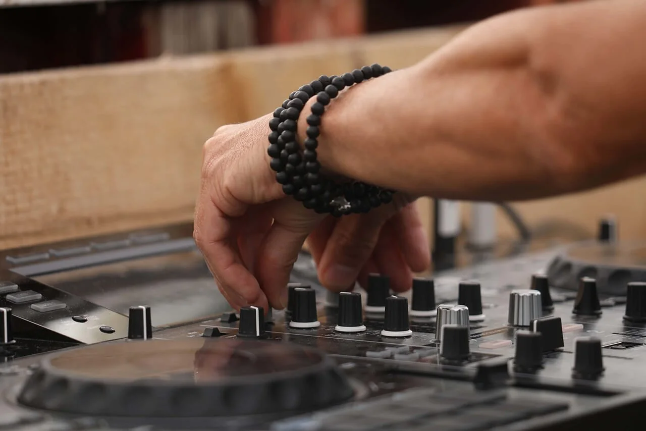Lors d’un événement, la main d’un DJ ajuste les réglages de la table de mixage, créant une ambiance vibrante.  Le style photographique de François Fauré capture l’énergie de ces événements, mettant en valeur les couleurs et le décor.  Un gros plan su