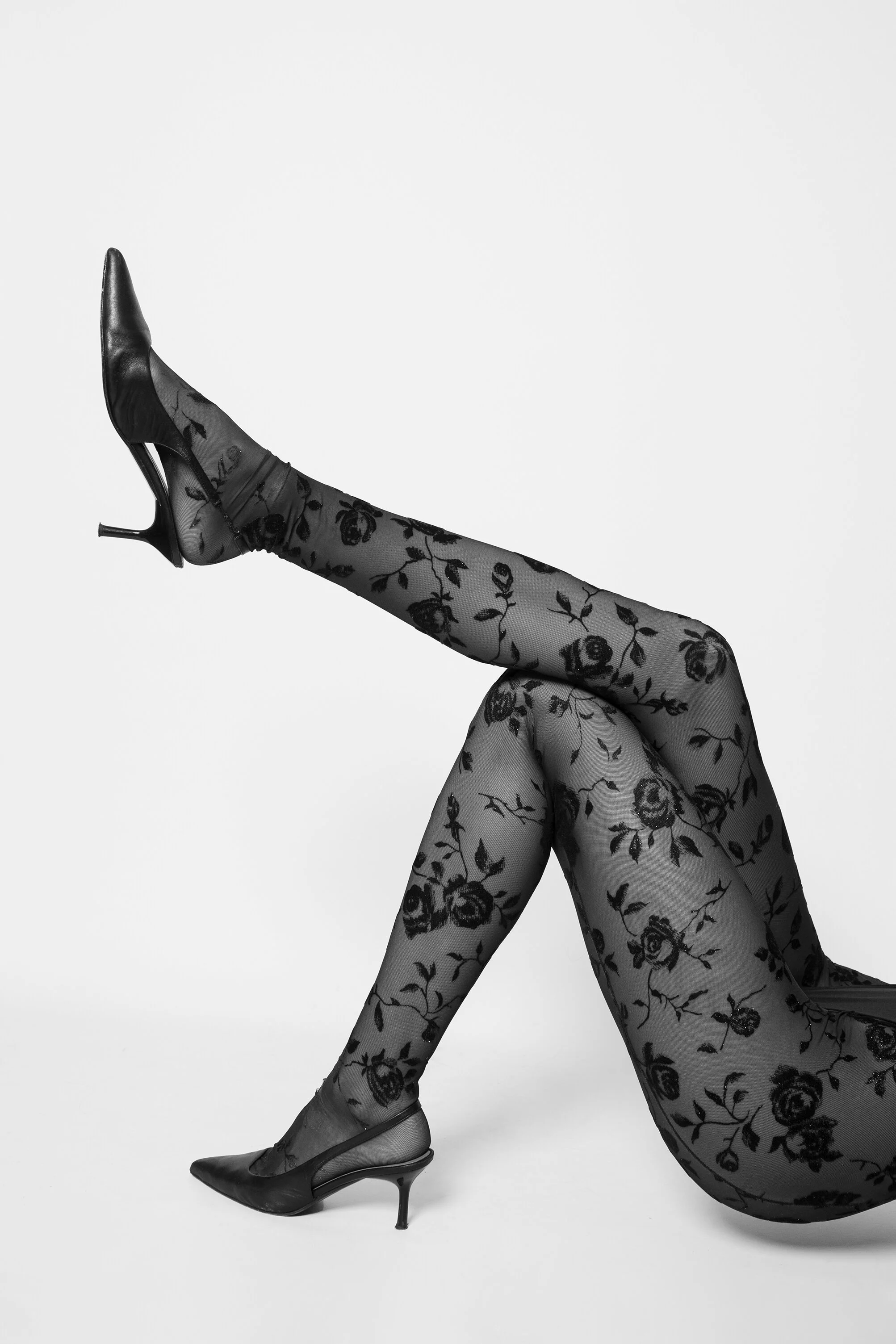 Jambes féminines portant des collants en dentelle avec un motif floral, chaussées de talons hauts en cuir