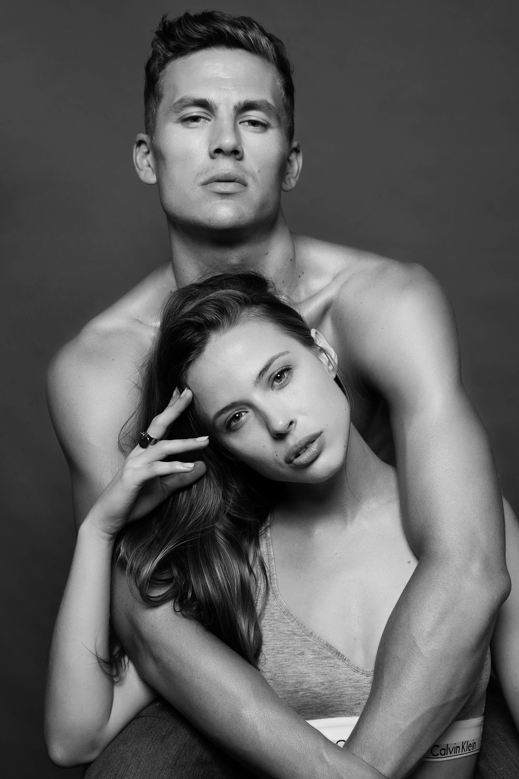 Un homme et une femme sans vêtements apparents posent de manière artistique sur un fond gris, la photo est en noir et blanc.