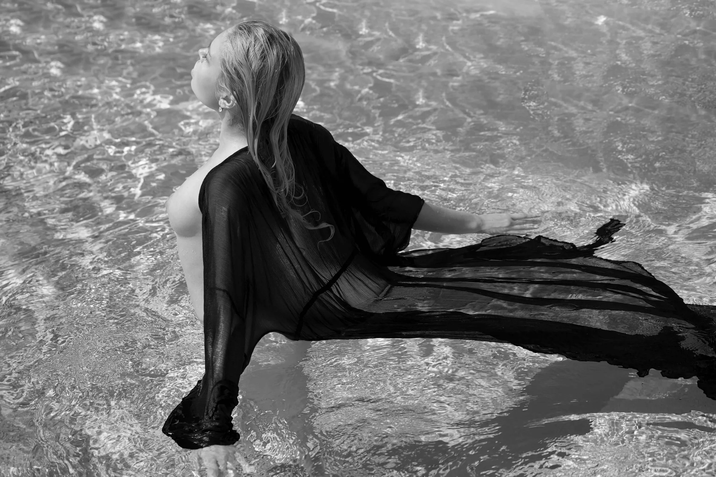 Femme allongée dans l'eau, portant un vêtement noir léger, avec les yeux fermés et le visage tourné vers le haut.