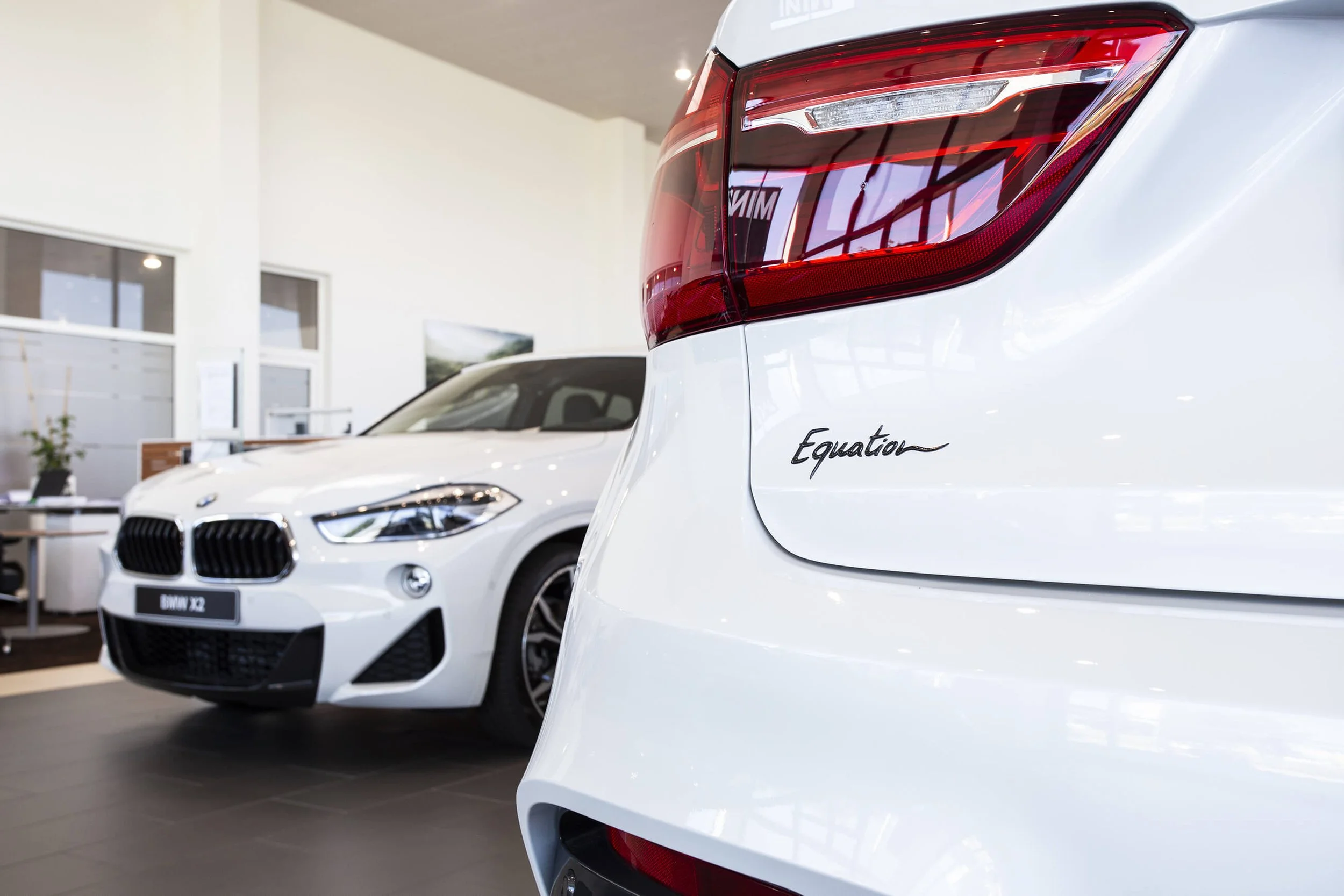 Photographie professionnelle d’une voiture dans un showroom moderne.  Détails du style photographique de François Fauré pour les voitures, mettant en avant un décor lumineux et moderne.  Palette de couleurs des voitures blanches dans un environnement