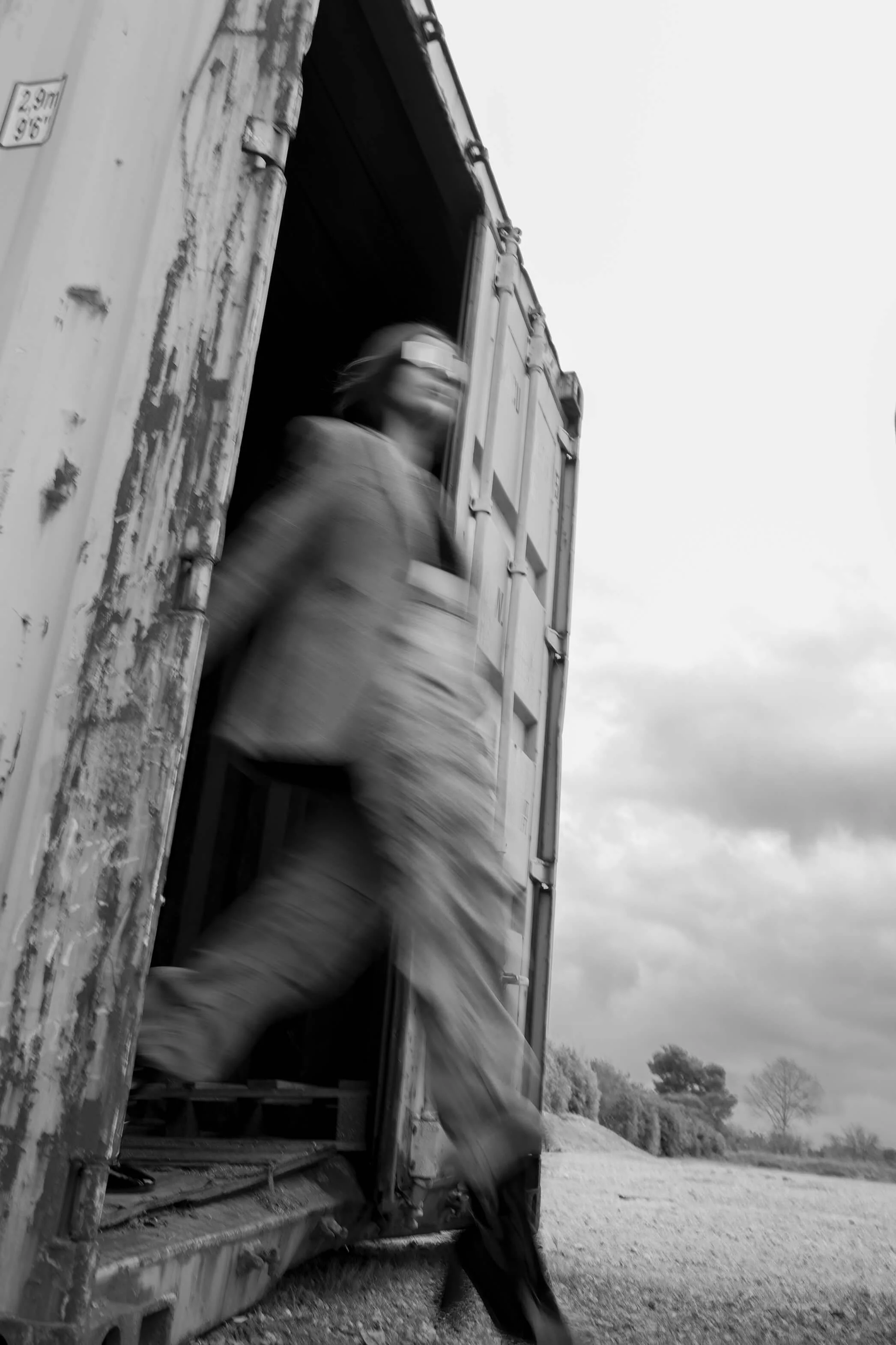 Main encore dans un train, homme en uniforme et casque, sortant de la porte du train dans un paysage rural, ciel nuageux.