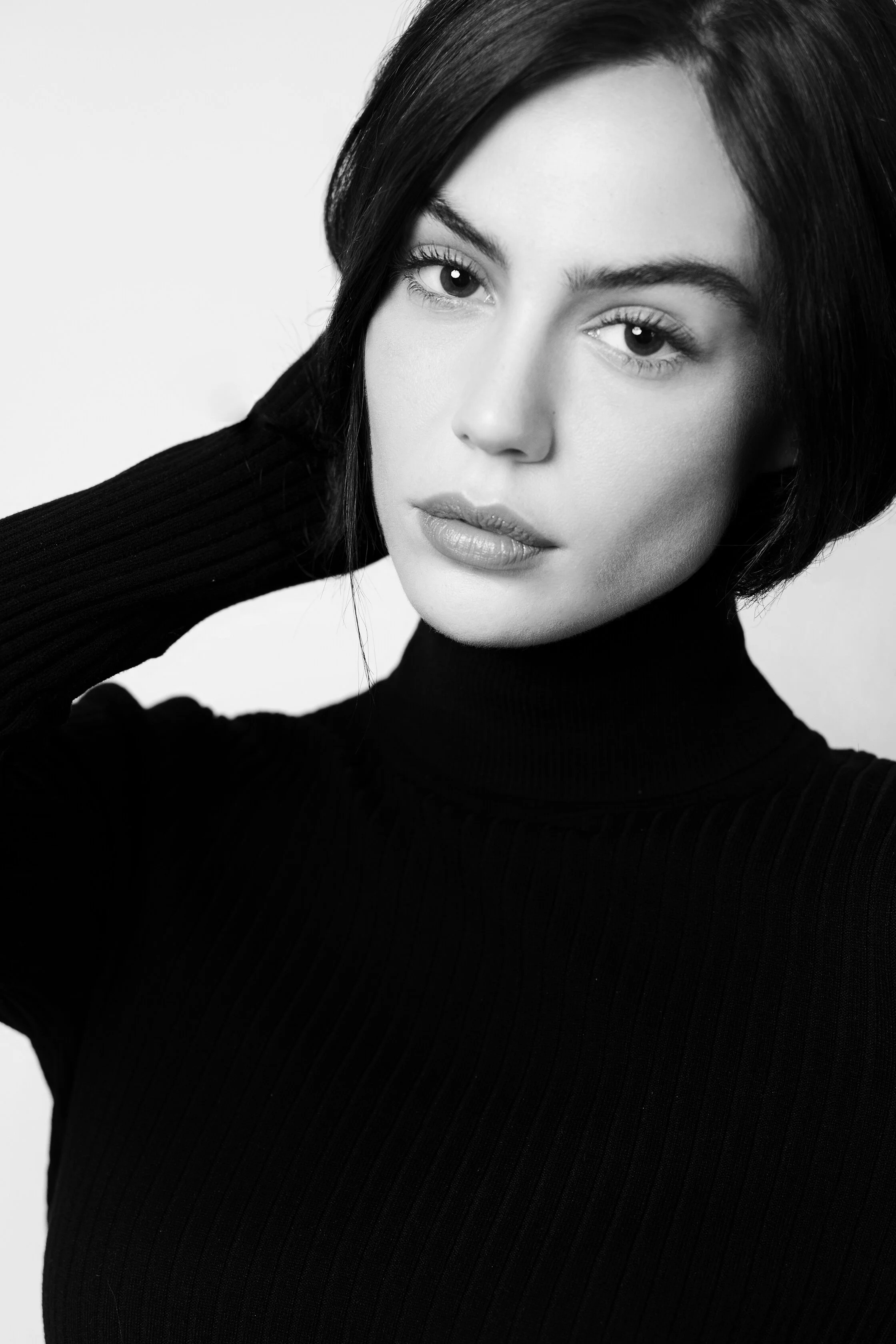 Portrait noir et blanc d'une femme aux cheveux courts, portant un pull à col roulé, regardant vers l'appareil.