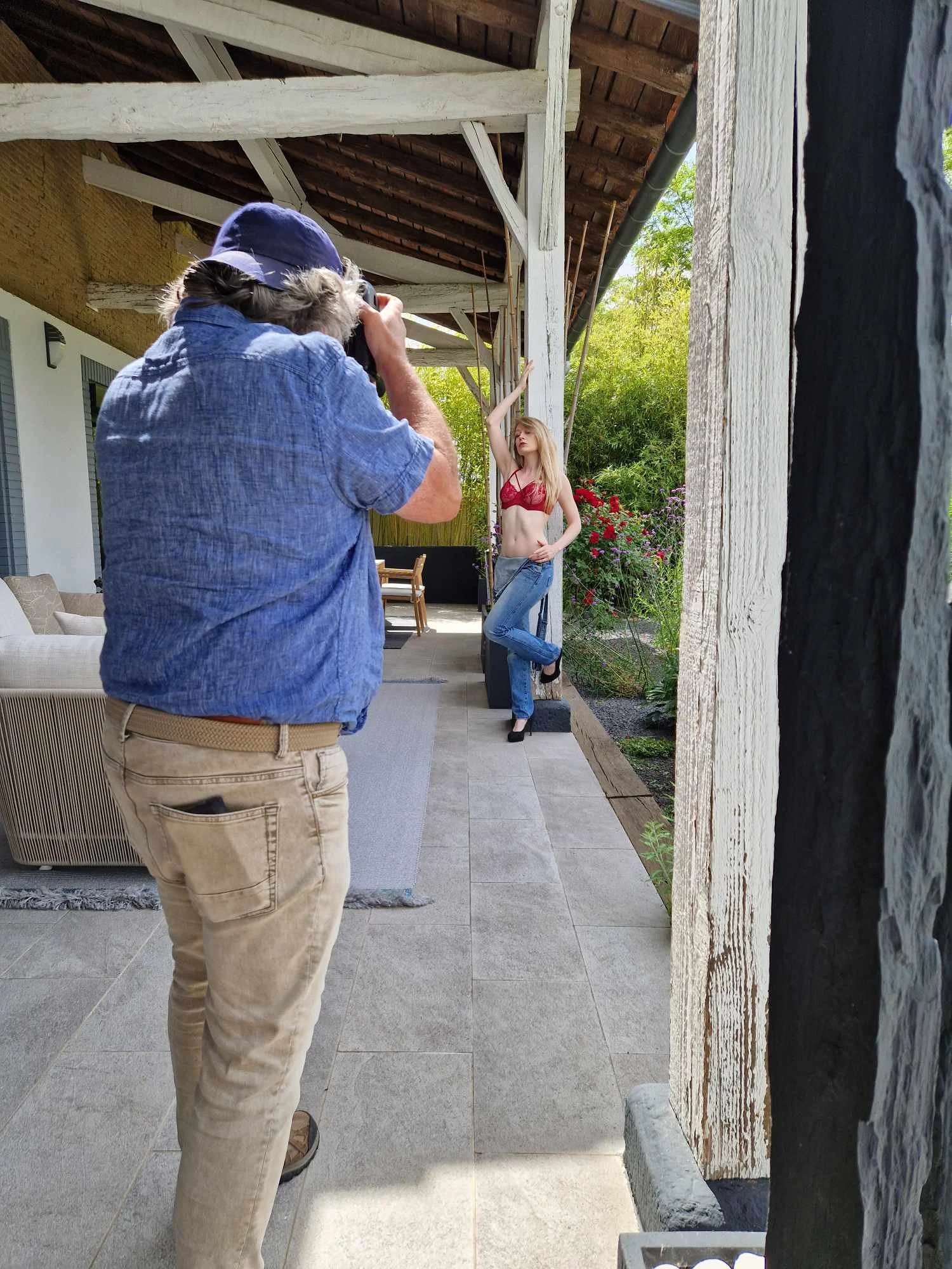 Un homme prenant une photo d'une femme posant contre une colonne extérieure dans un jardin ensoleillé.