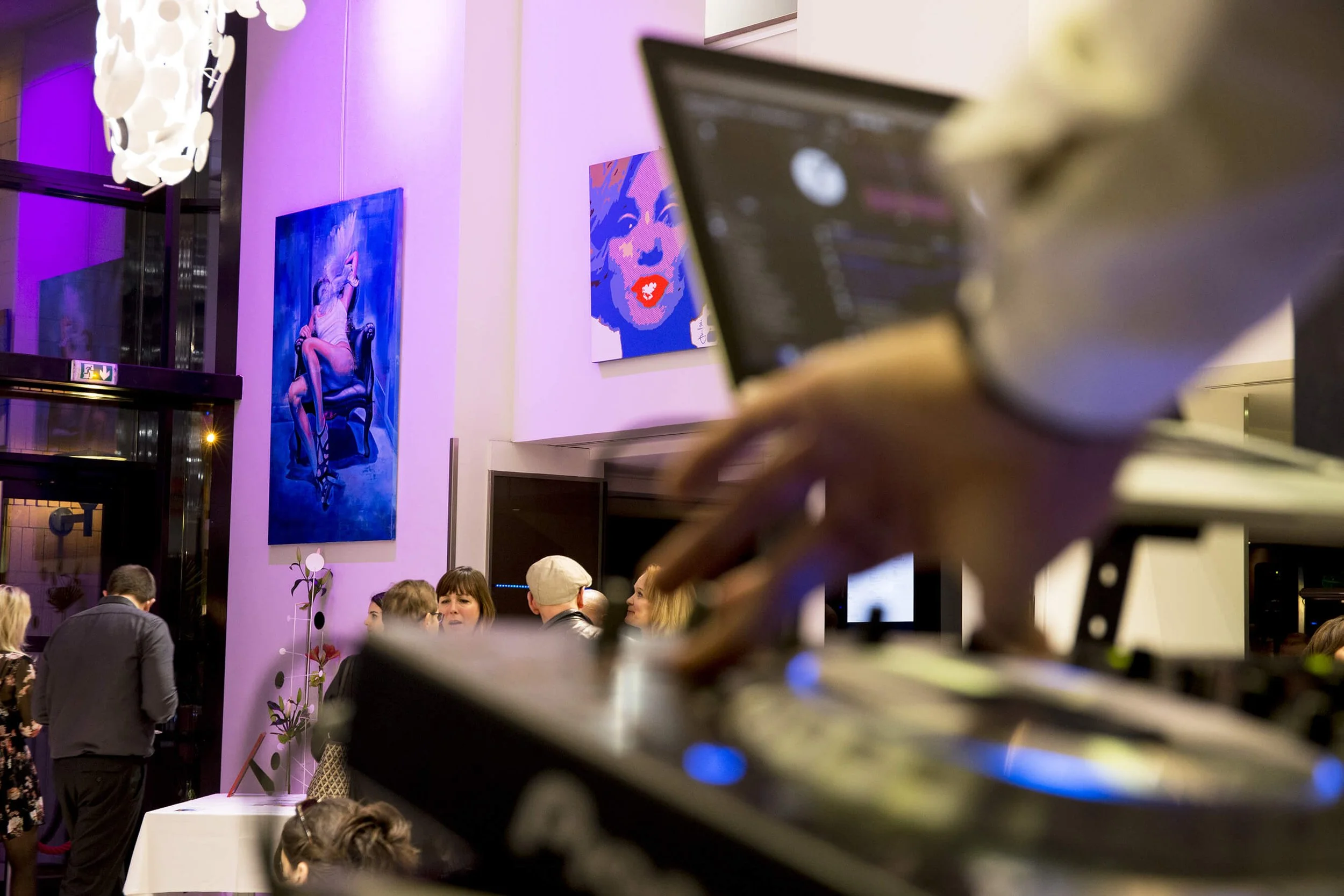 Des œuvres d’art colorées et un DJ en action créent une ambiance vibrante lors d’un événement nocturne. L’éclairage violet et la décoration artistique ajoutent une touche d’élégance.  Le style photographique de François Fauré capture l’interaction so