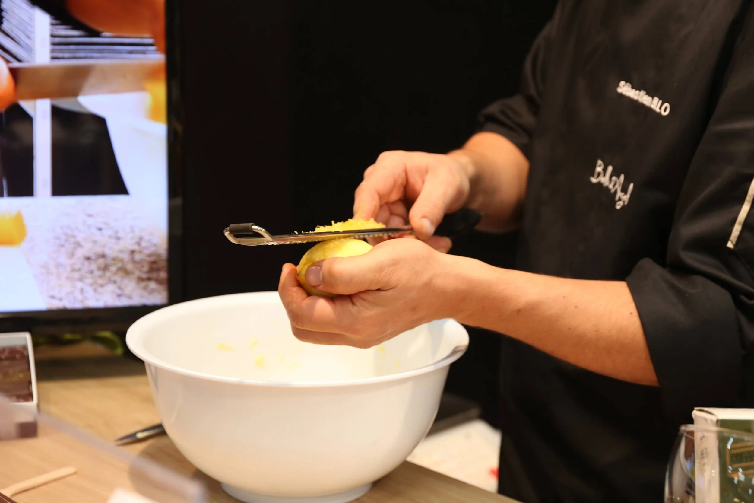 Dans un bol blanc immaculé, un chef professionnel râpe un citron, révélant son style culinaire unique.