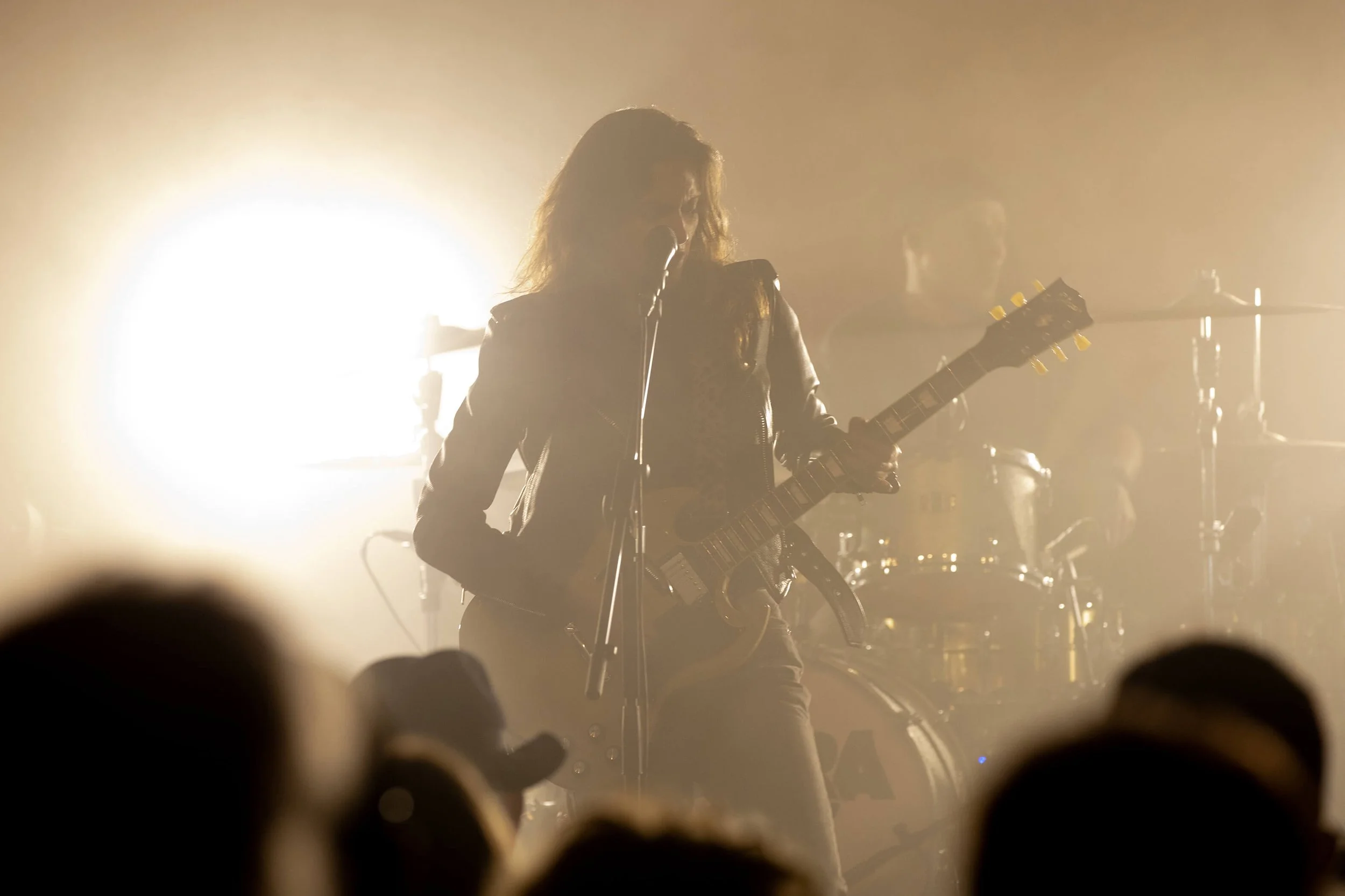 Photographie d’un concert rock avec une ambiance sombre et des lumières vives. Un musicien en performance sur scène joue de la guitare électrique.  Le photographe François Fauré capture l’énergie du moment. Le jeu de lumière et d’ombres crée une ambi