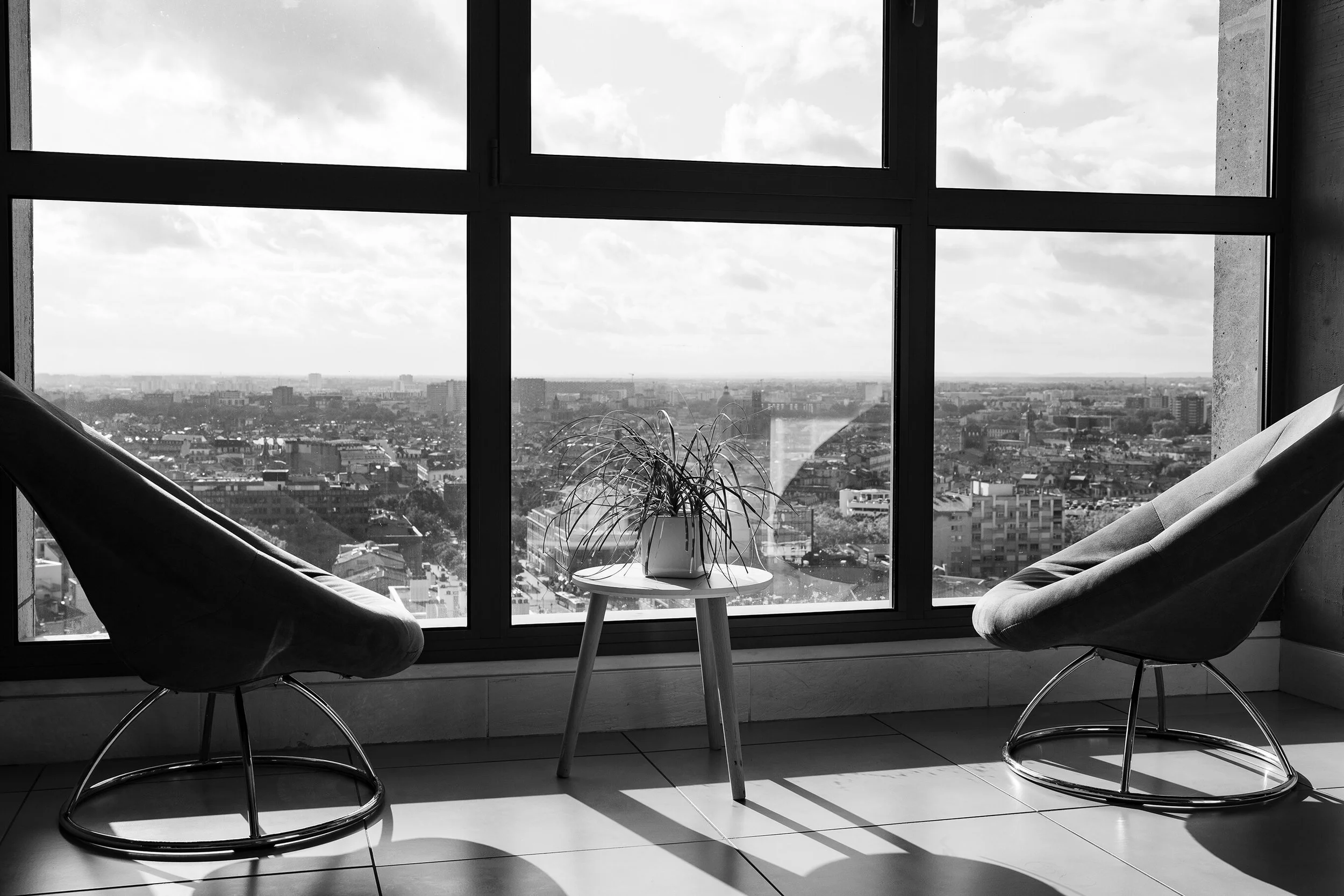 Un appartement moderne offre une vue panoramique imprenable, agrémentée d’élégantes chaises et d’une plante verdoyante.  L’ambiance minimaliste en noir et blanc d’un espace de travail professionnel respire la sophistication.  Le style photographique 
