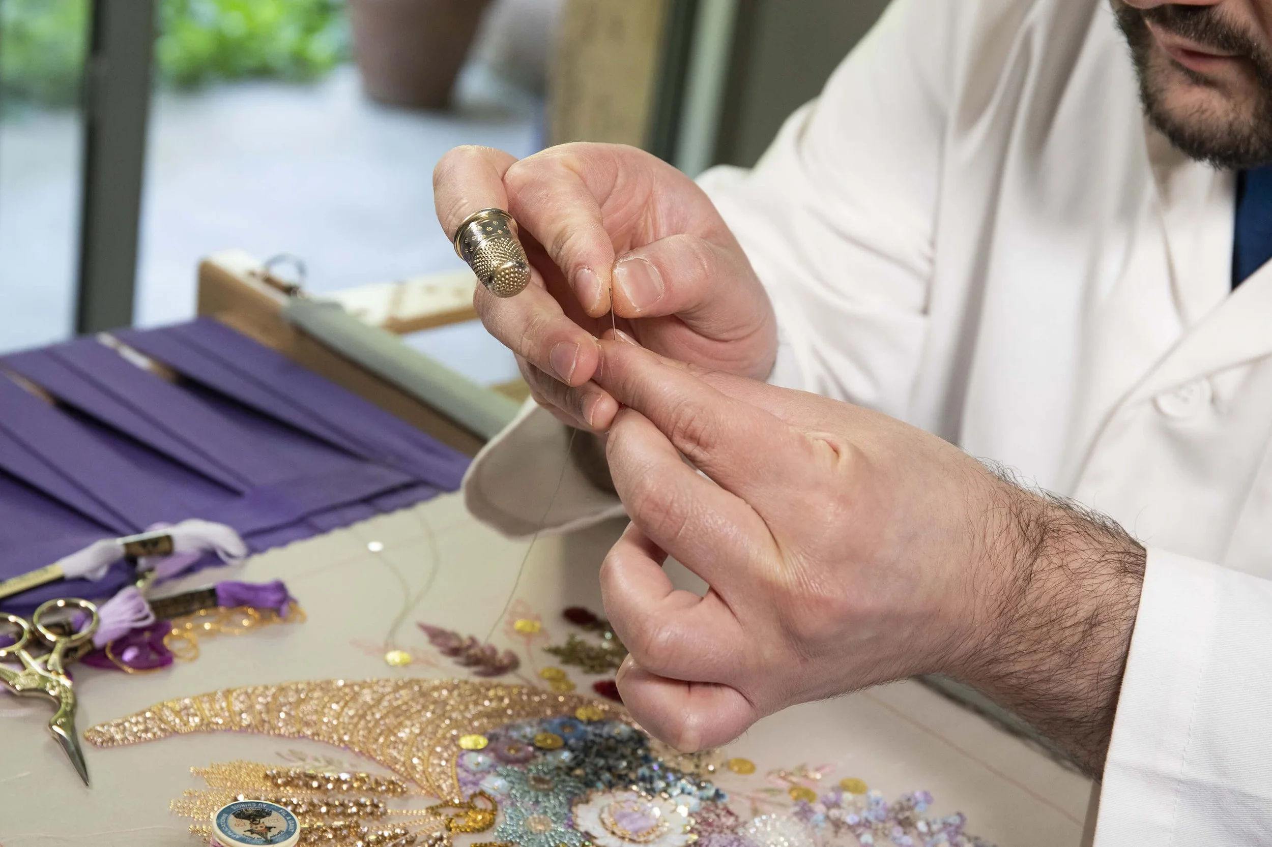 Dans un atelier de couture, un artisan démontre avec expertise des techniques de couture complexes, utilisant des perles et des fils pour créer des œuvres d’art captivantes.  Un photographe professionnel immortalise avec soin le travail minutieux de 