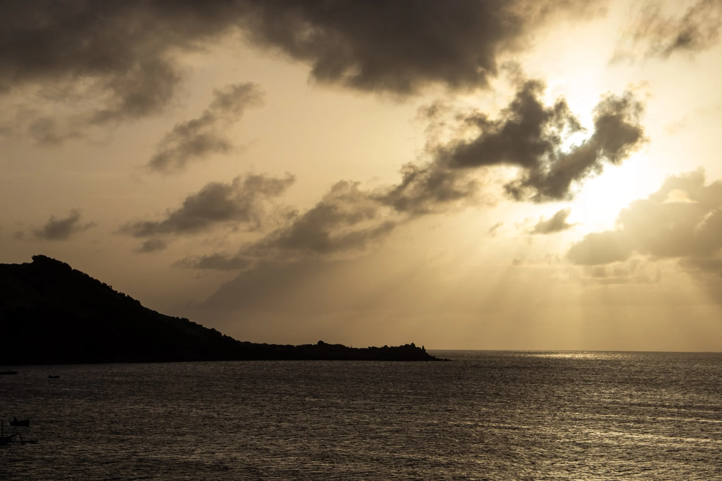 Sunset over the ocean with dark clouds and a mountain on the left side.