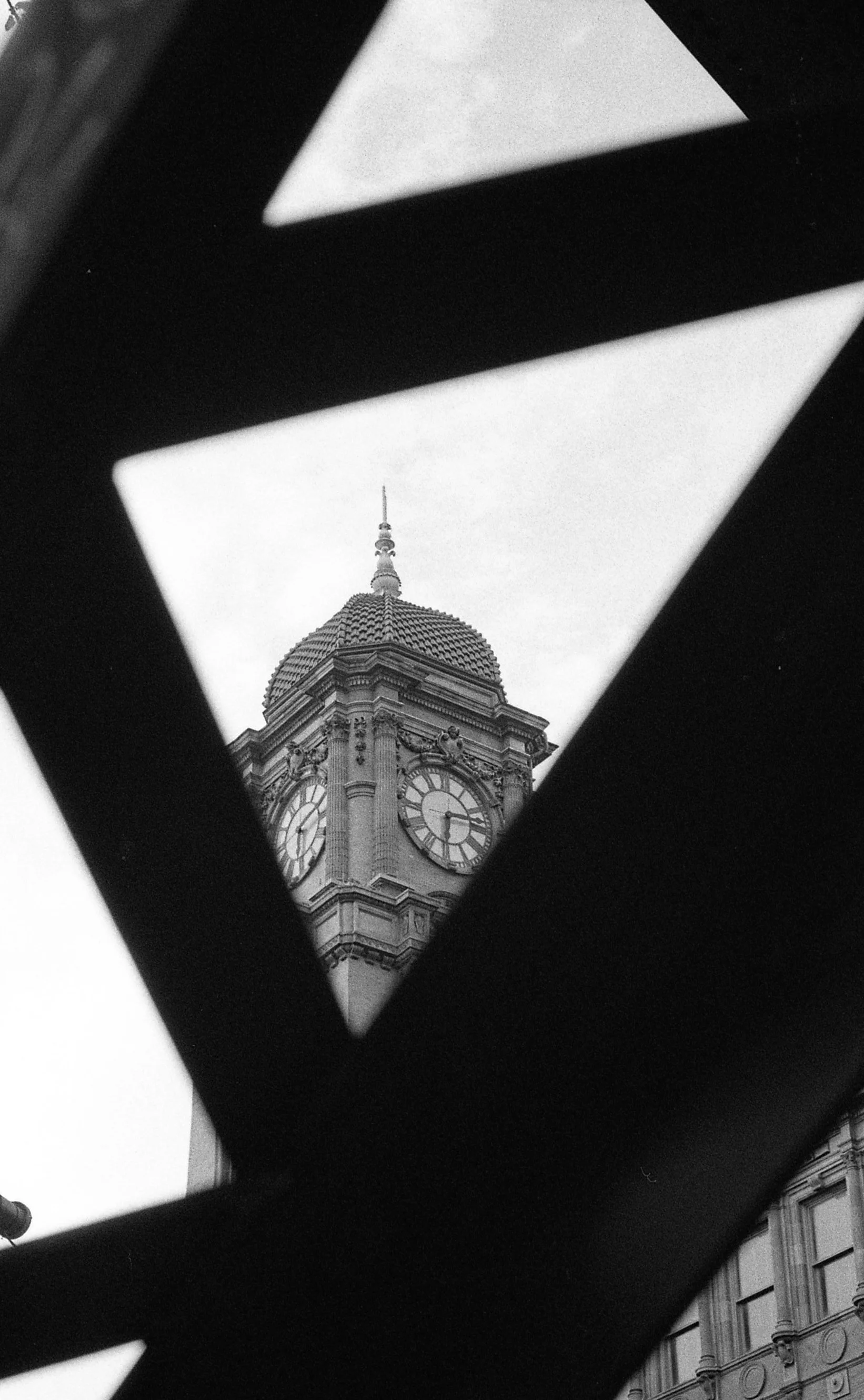 View of a clock tower with a domed roof seen through a geometric cutout in a dark structure.