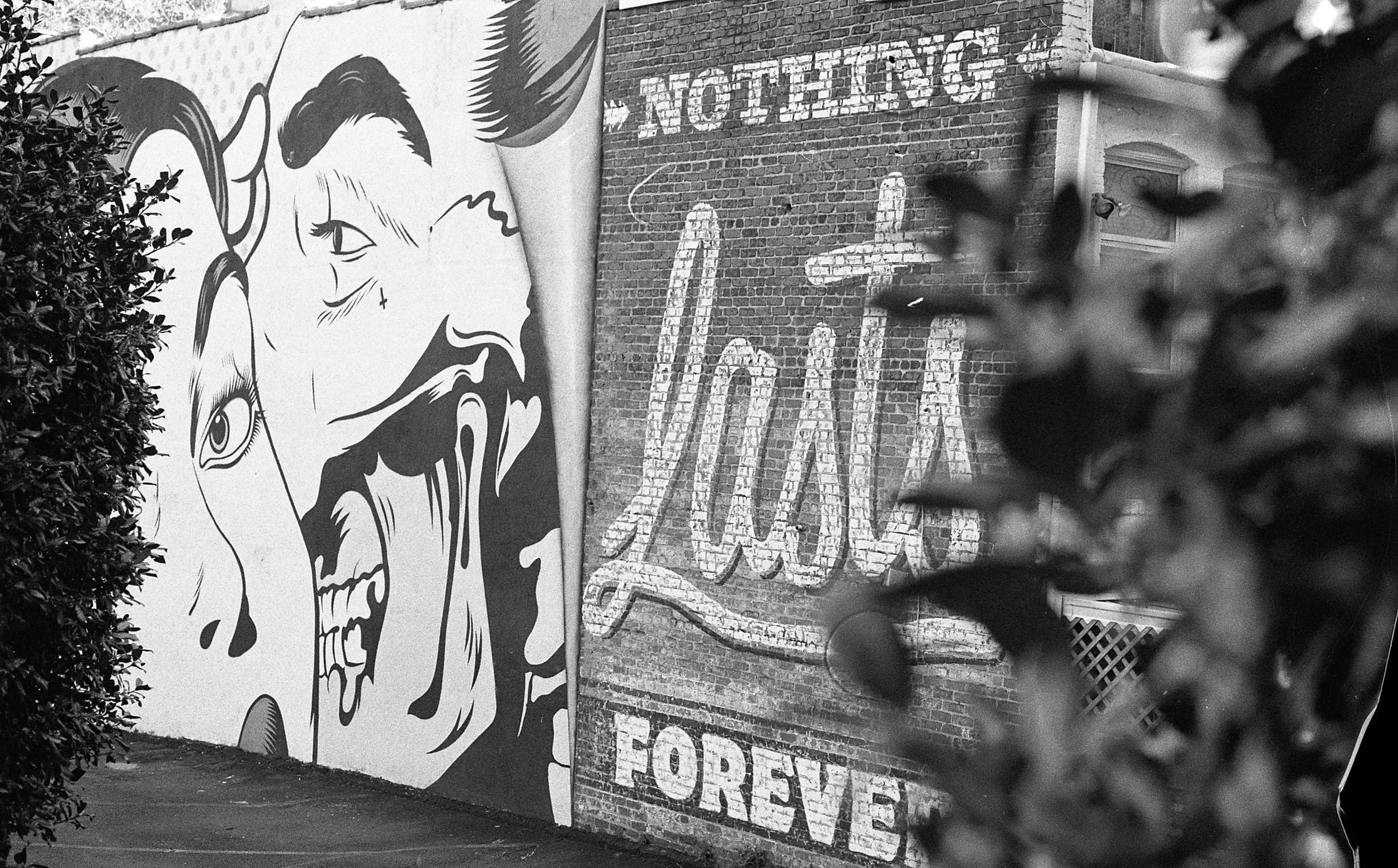 Street art on brick wall featuring stylized portraits of a woman and a man, with words 'Nothing' and 'Love' written in large graffiti-style lettering, and the word 'Forever' at the bottom.