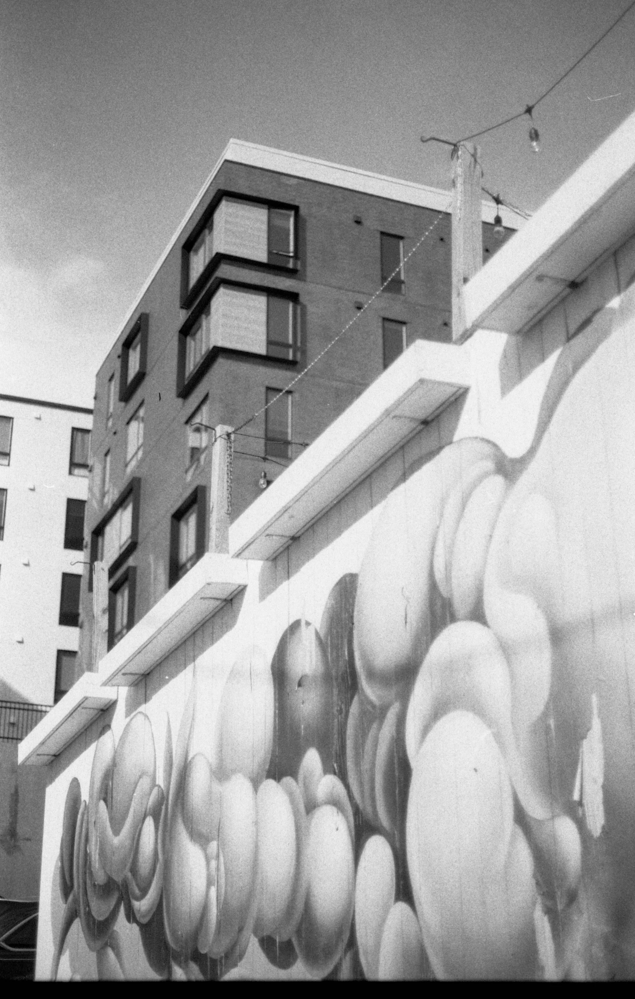 Black and white photo of a modern apartment building with graffiti art on a wall in the foreground.
