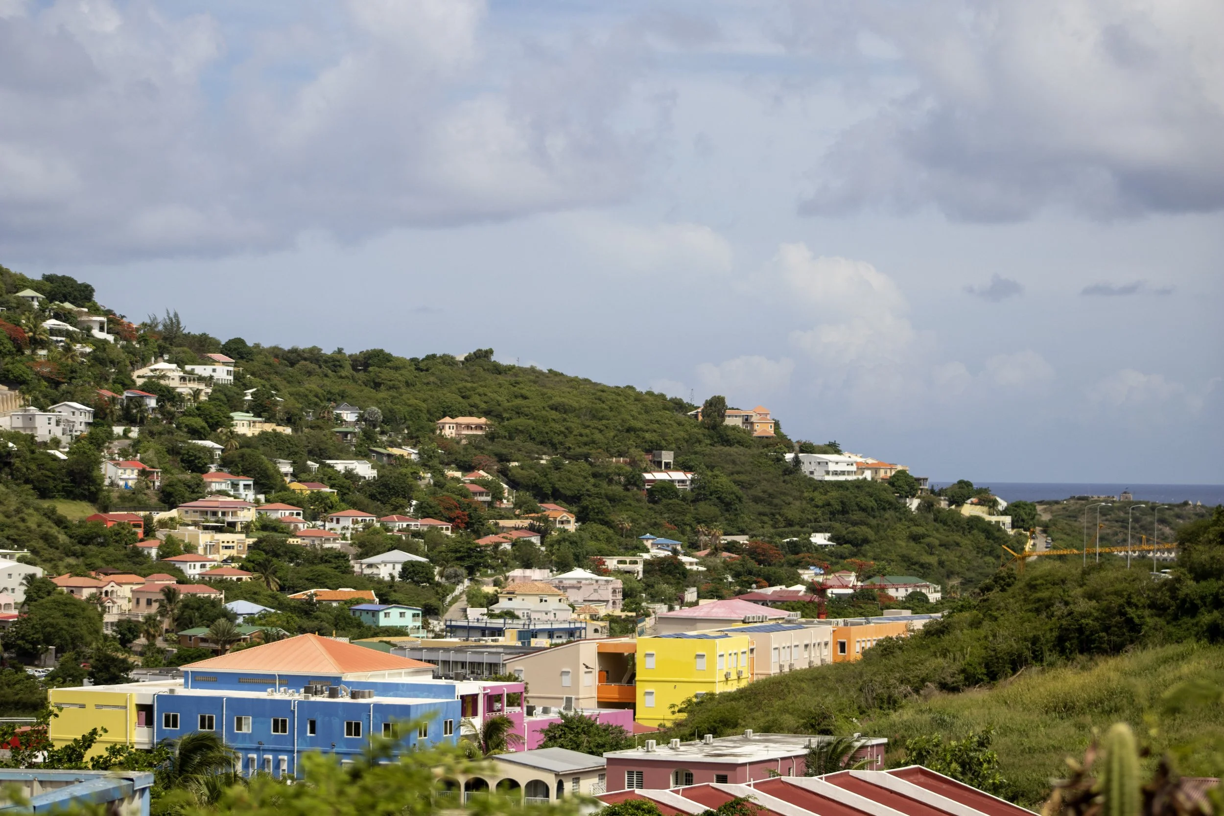 Colorful buildings on a hillside with a cloudy sky and the ocean in the background.