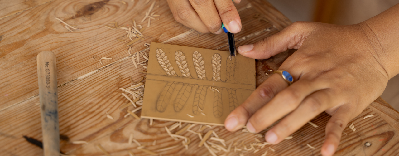 Person carving leaf patterns into a linoleum slab for block printing.