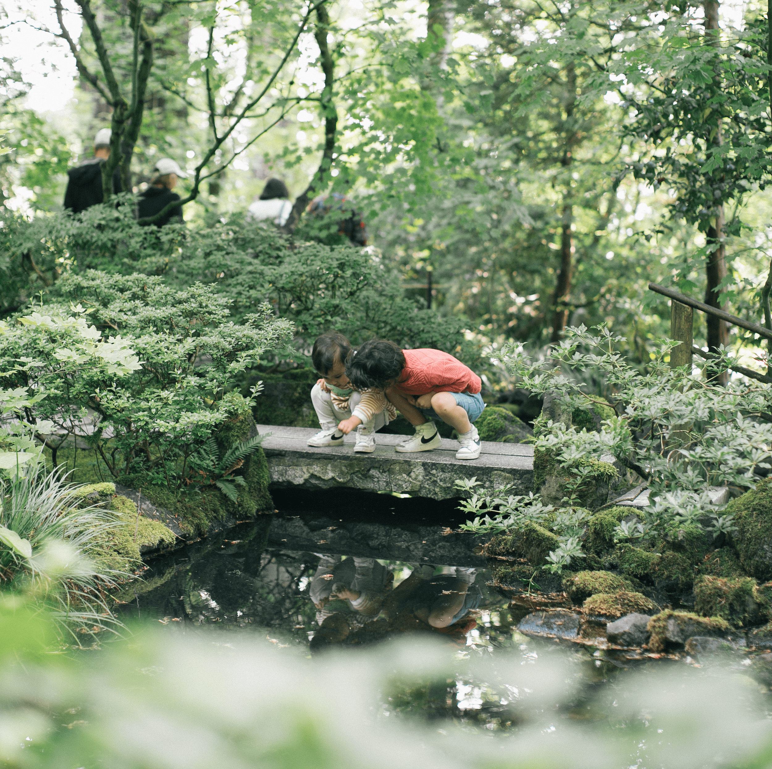 Two children exploring a stone bridge over a koi pond at the Portland Japanese Garden
