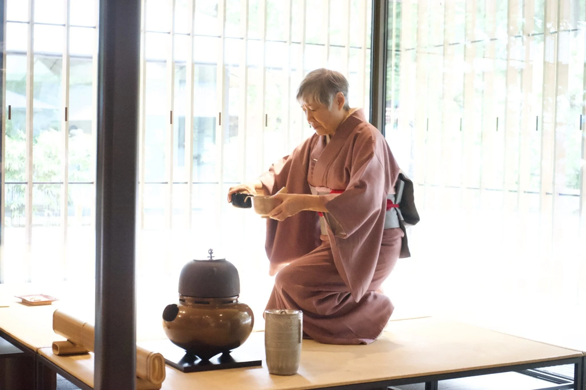  A tea master in kimono prepares matcha on the tatami floor. 