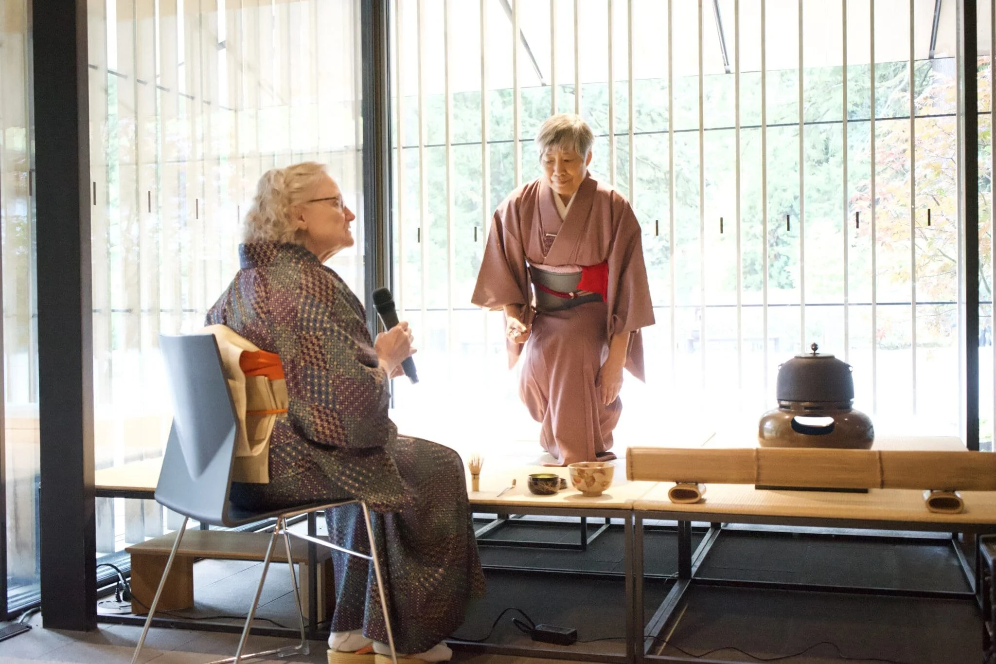  A tea practitioner kneels at the tea setup as guests look on at Portland Japanese Garden. 