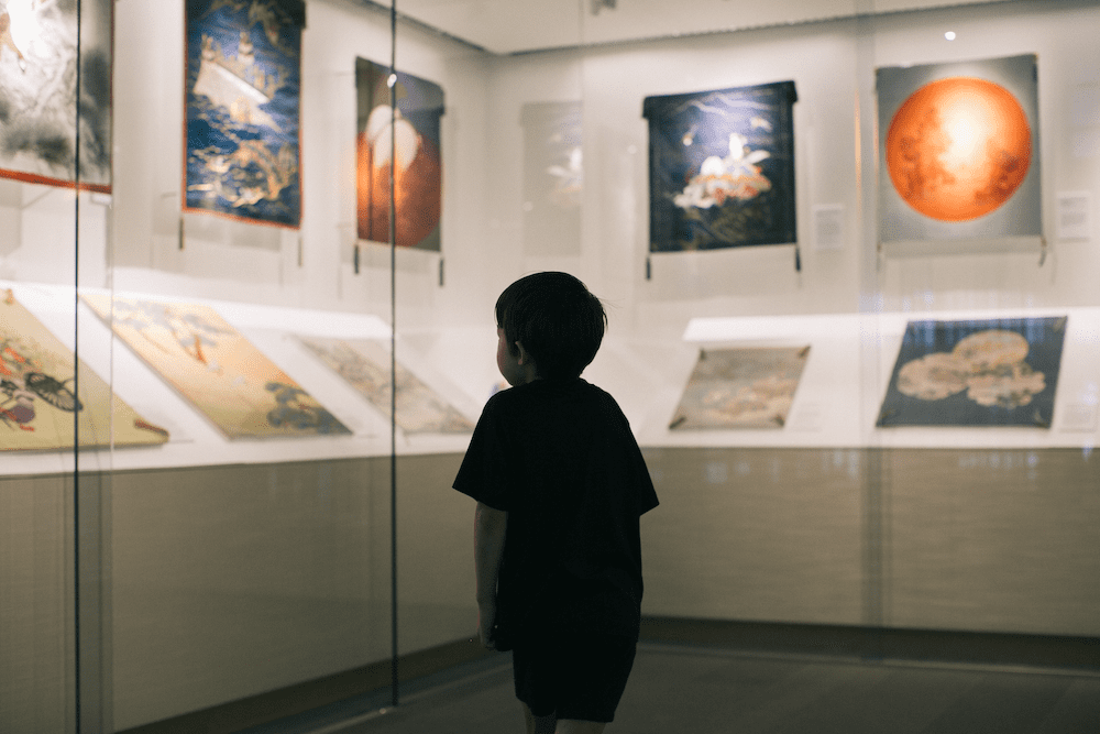 A young child looking at art exhibits displayed behind glass walls.