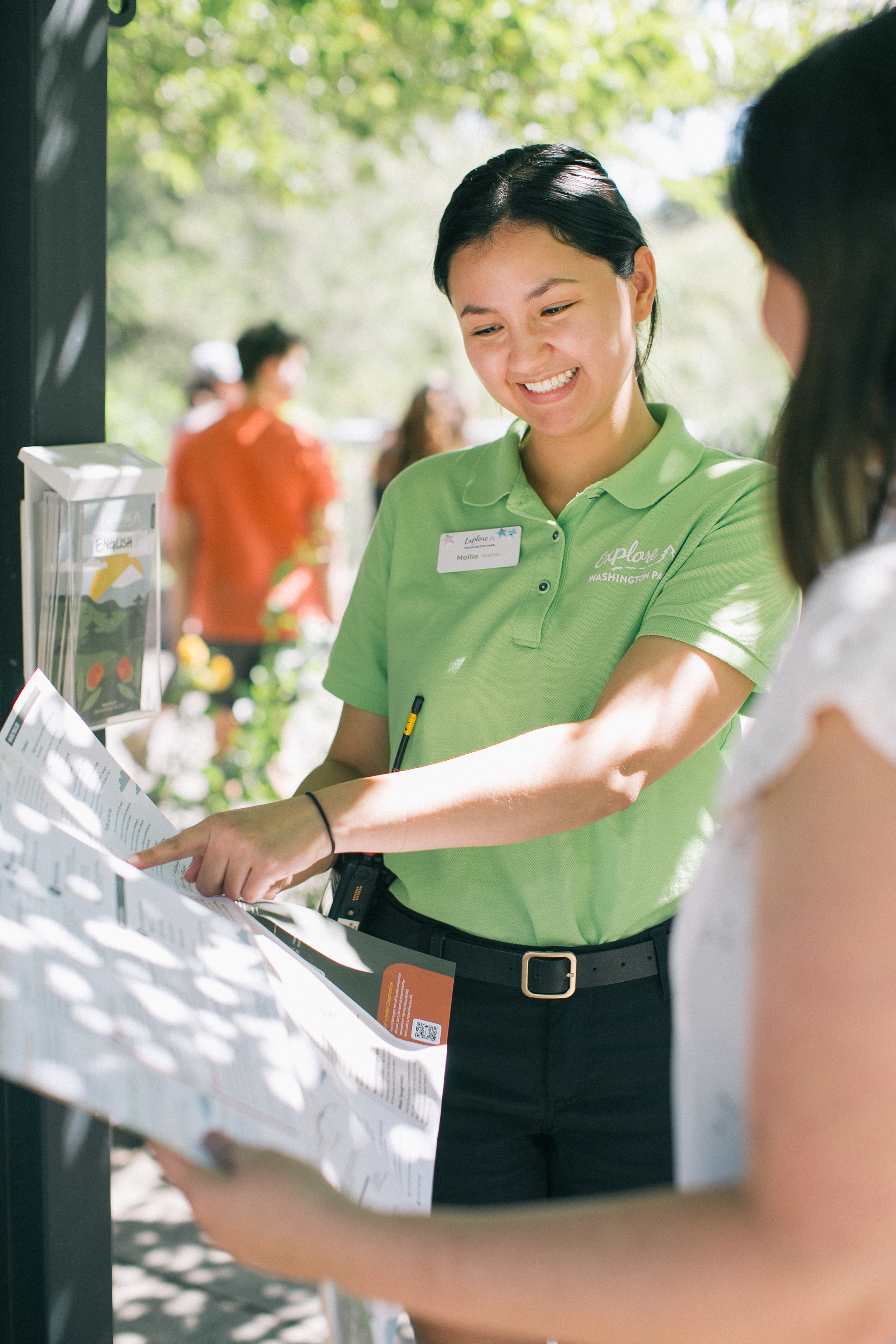 A Washington Park staff member helping visitors outdoors, next to common questions about visitor services.