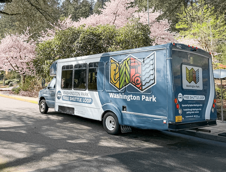 The Washington Park Free Shuttle Loop bus parked near blooming cherry trees, with the Washington Park logo artwork on the side