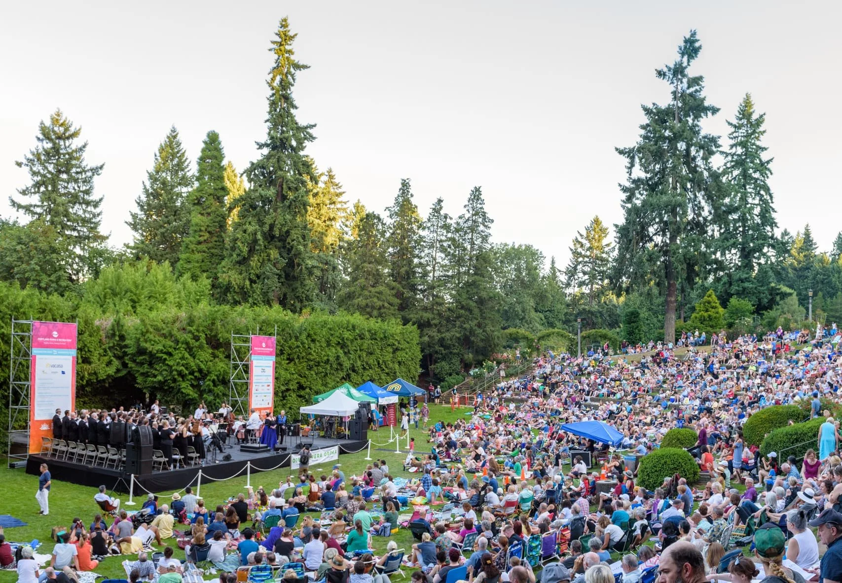A large outdoor summer concert at Washington Park with hundreds of attendees on the lawn and a performance stage