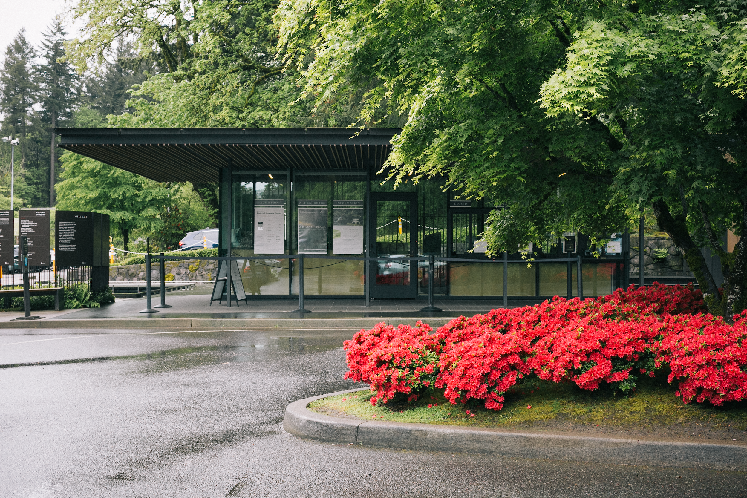 The Portland Japanese Garden front entrance features a  area with vibrant red flowers in a raised planter in front of the entrance which has large glass windows and doors.