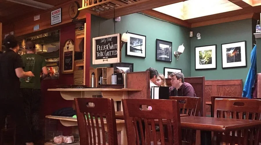 The cozy interior of Leaky Roof Gastro Pub in Portland, with dark wood furniture, framed photos on green walls, and diners at the bar