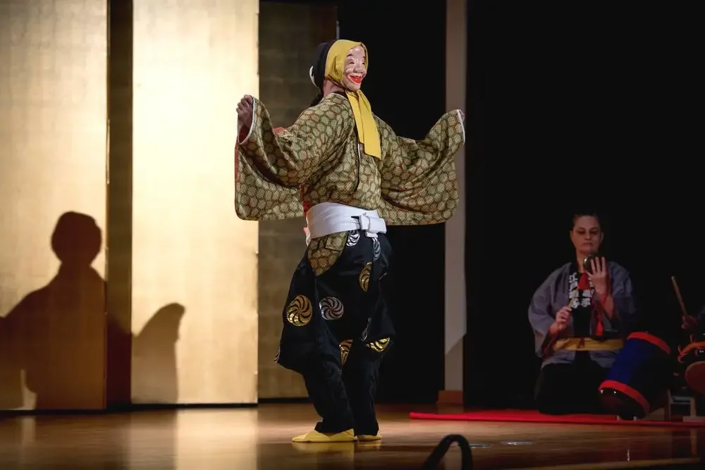 A dancer performs the Ryomen Odori double-masked dance wearing the smiling Okame mask.