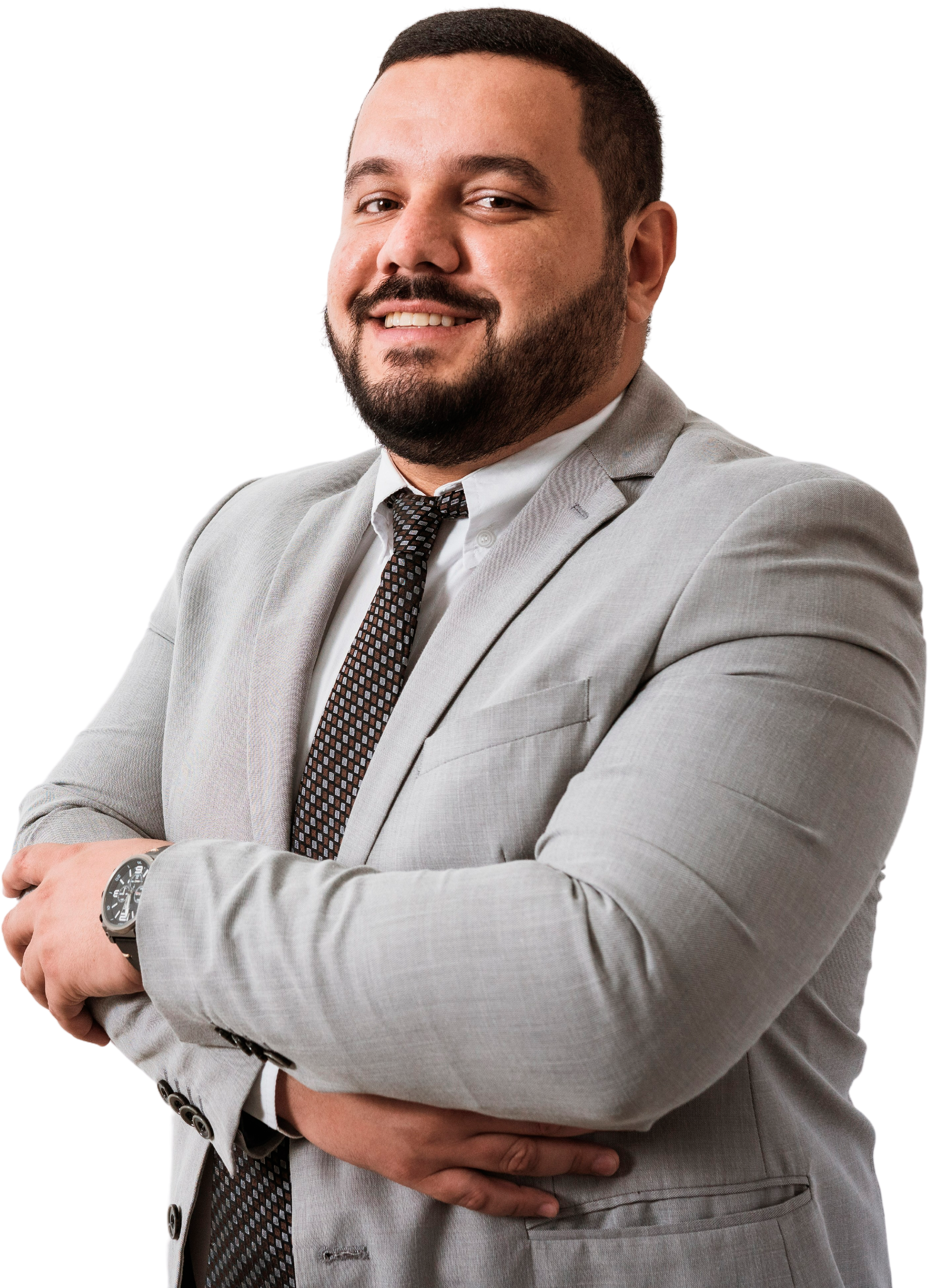 A man wearing a light gray suit with a white shirt and a patterned tie, smiling with arms crossed, in front of a plain background.