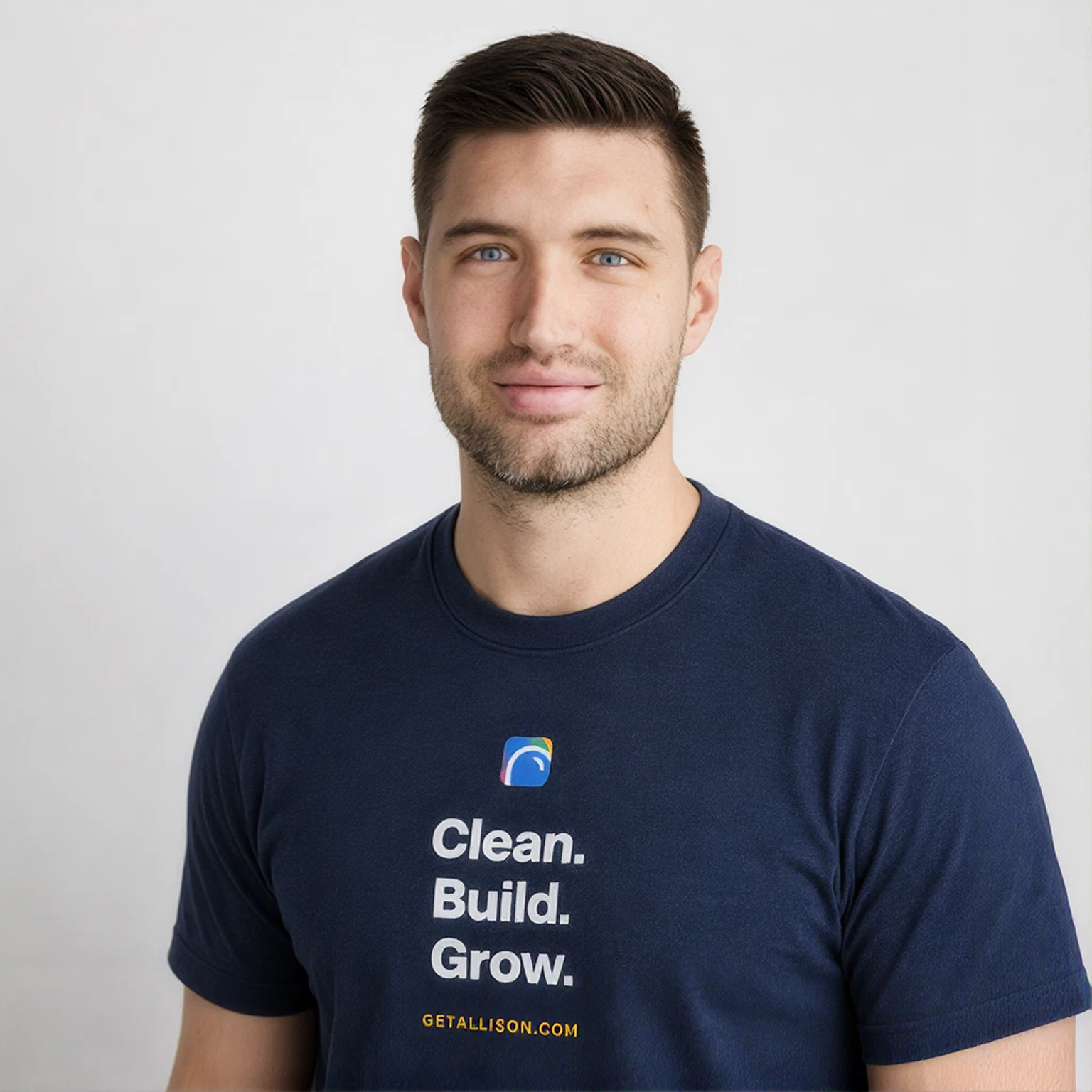 A young man with short brown hair and blue eyes wearing a navy t-shirt with the words 'Clean. Build. Grow.' and a logo on it, standing against a plain white background.