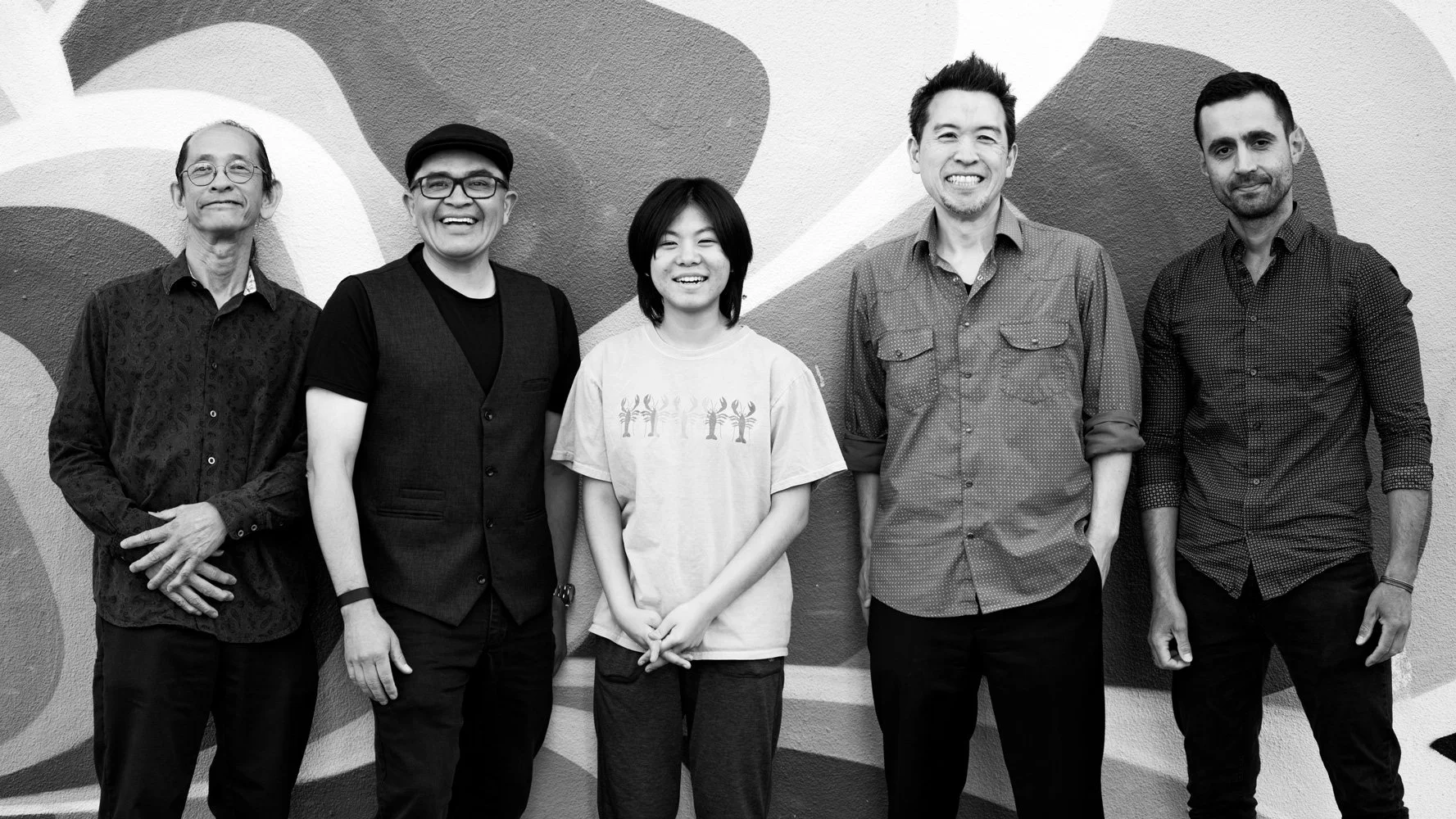 Five people standing side by side in front of a mural, smiling at the camera.