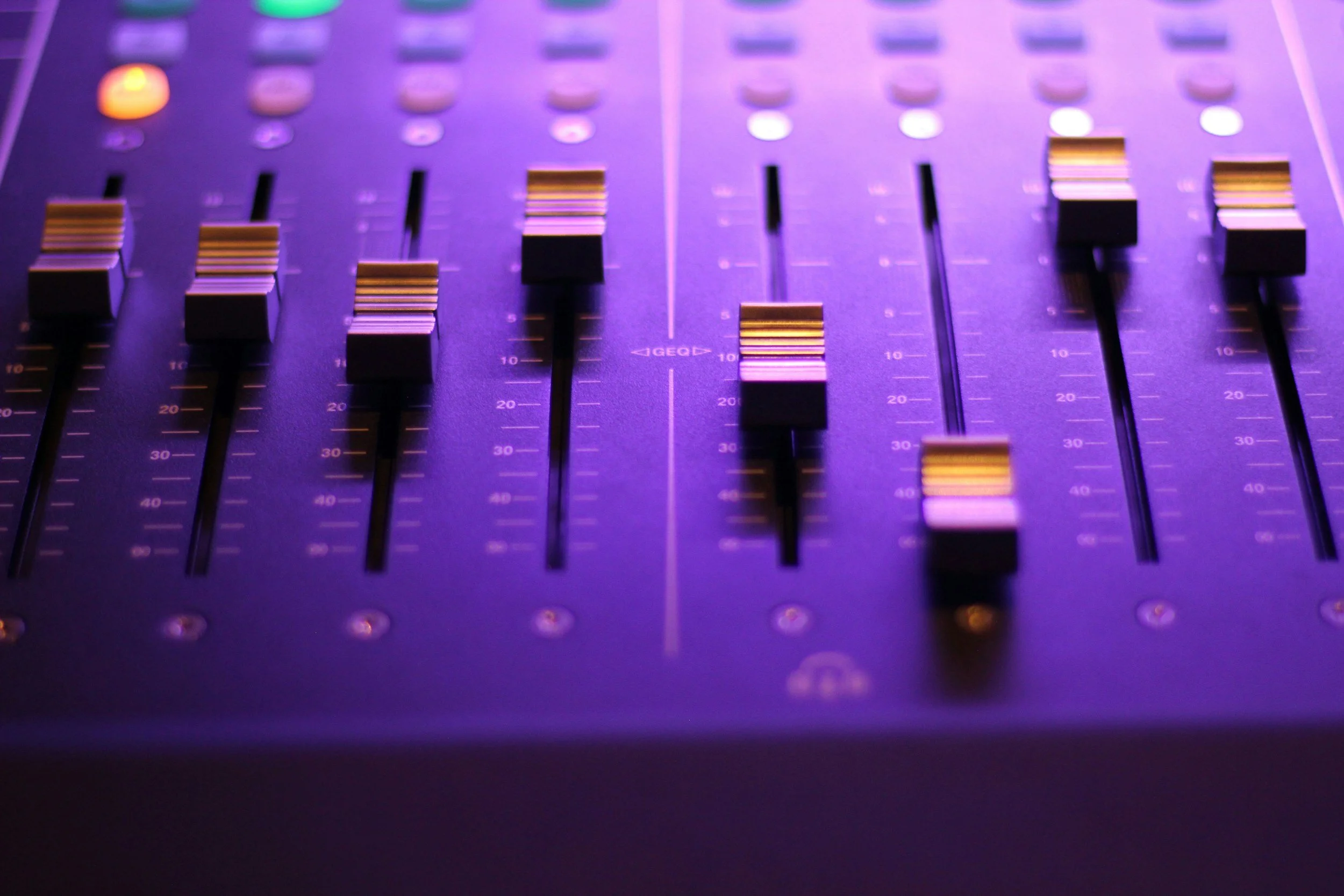 Close-up of an audio mixing console with purple and yellow lighting.